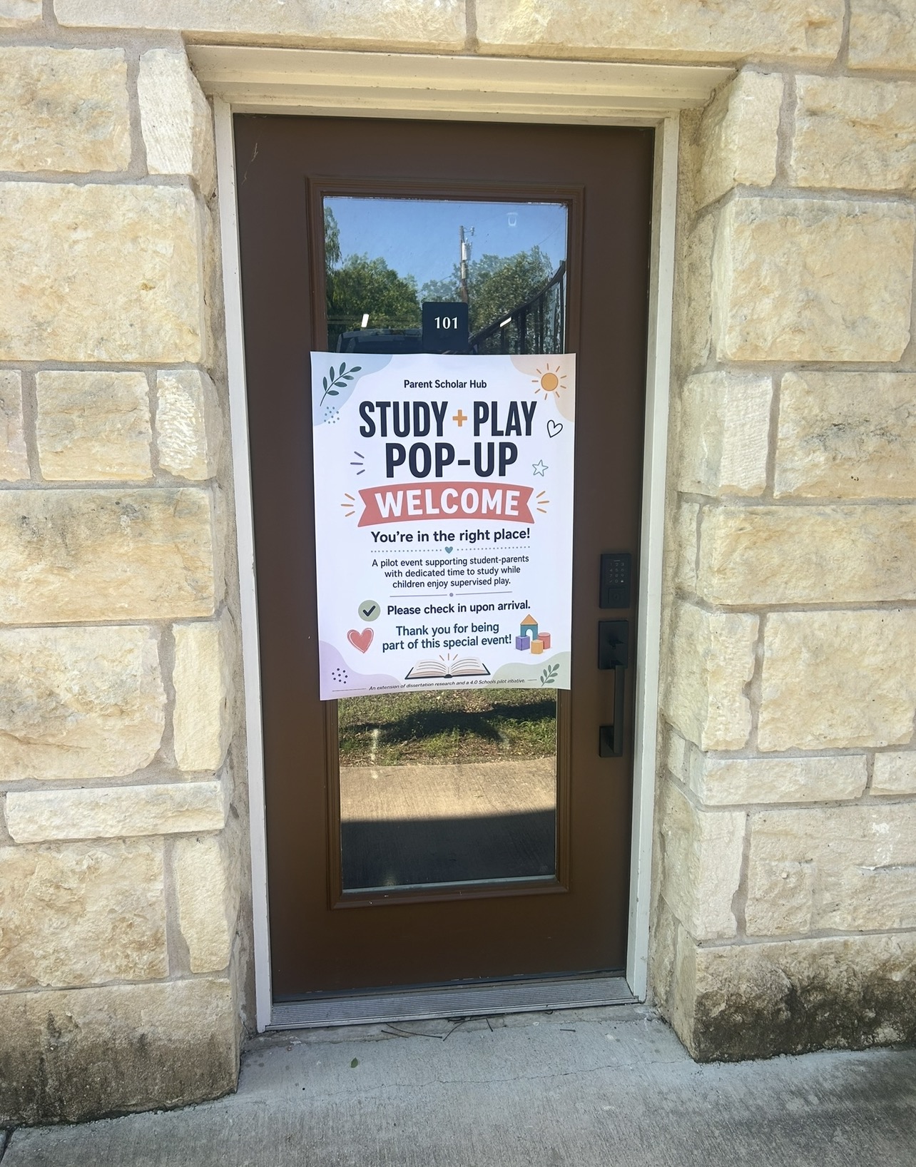 Door with a sign welcoming visitors to a study and play pop-up event, attached to a stone wall.