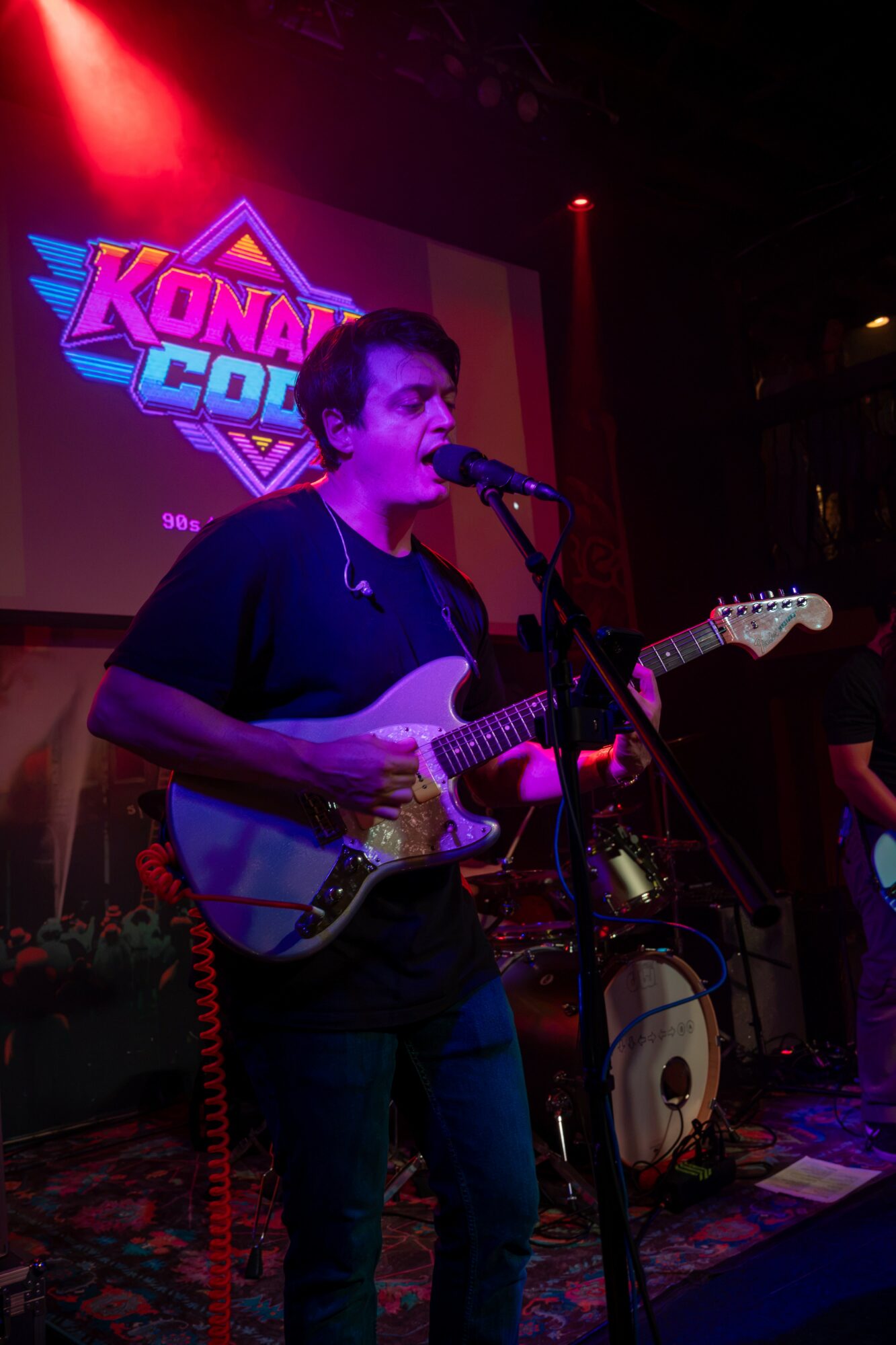 Person playing electric guitar and singing into microphone on stage with colorful background