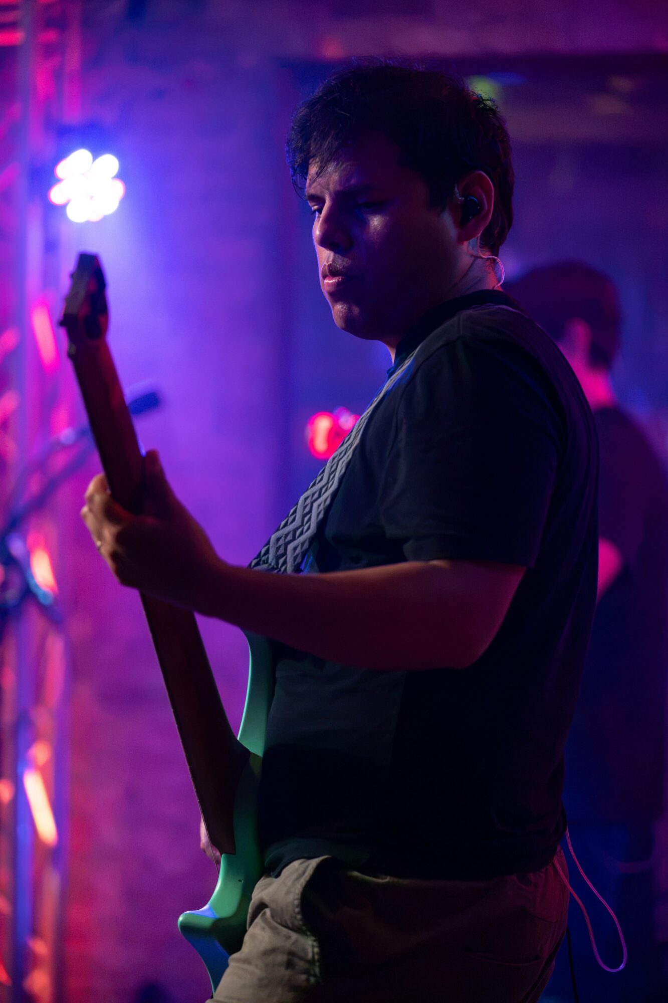 Young man playing guitar in a dimly lit setting with purple and blue lighting, focused on his instrument.