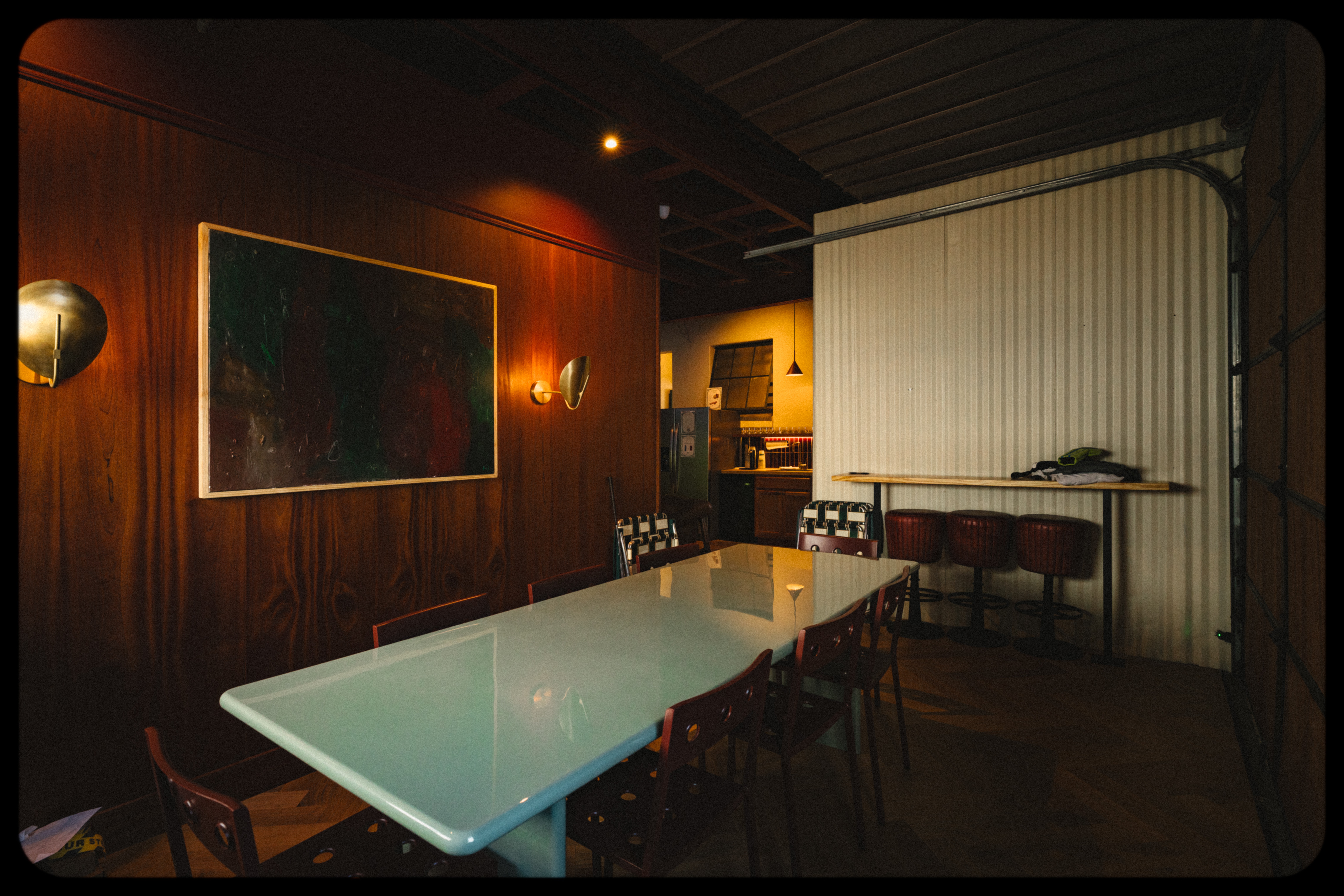 Dining room with a glass table, wooden chairs, a large framed mirror, and a bar area with stools, warm lighting.