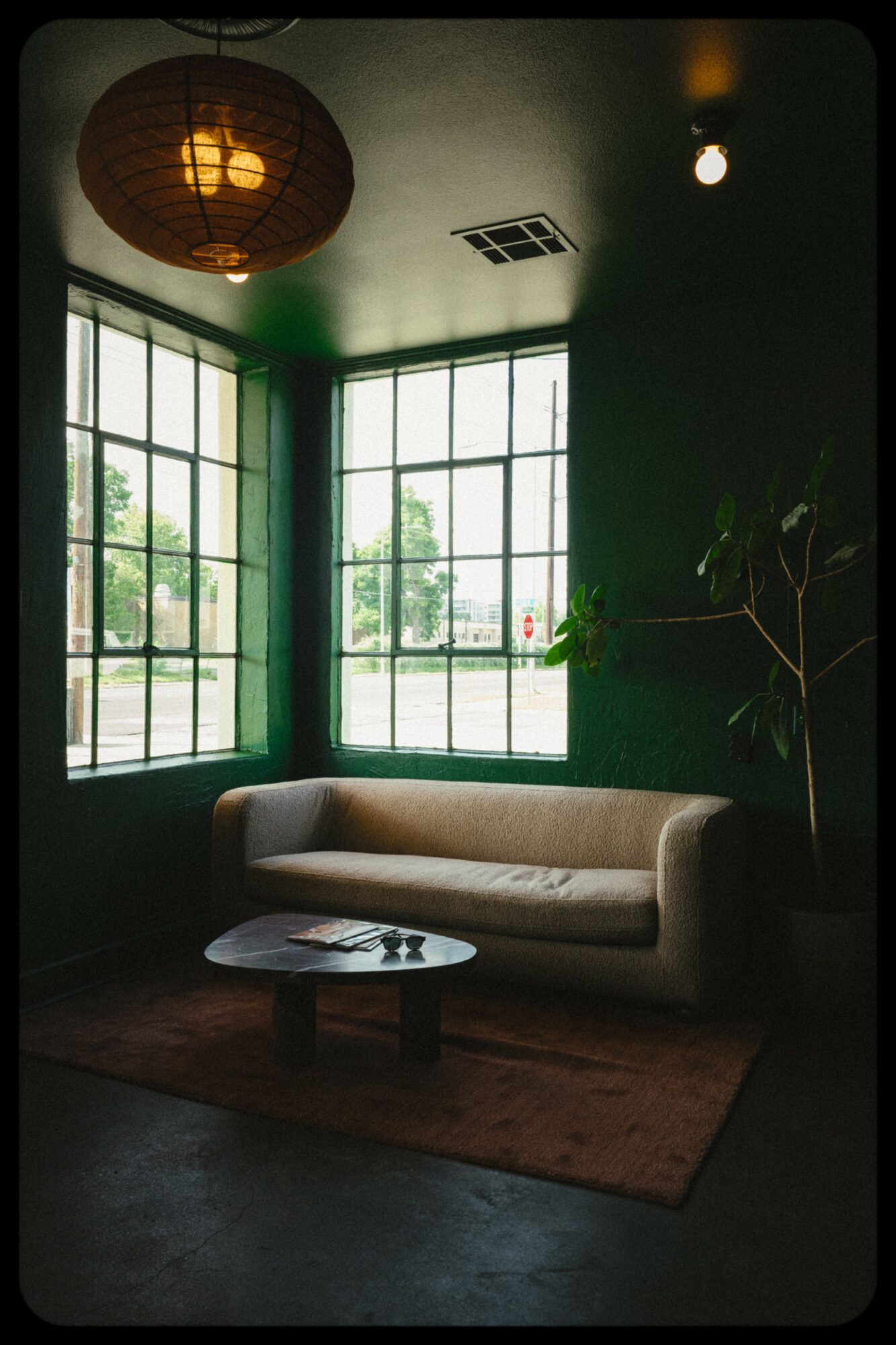 Cozy room with large windows, a beige sofa, a small round table, and a potted plant, illuminated by warm lighting.