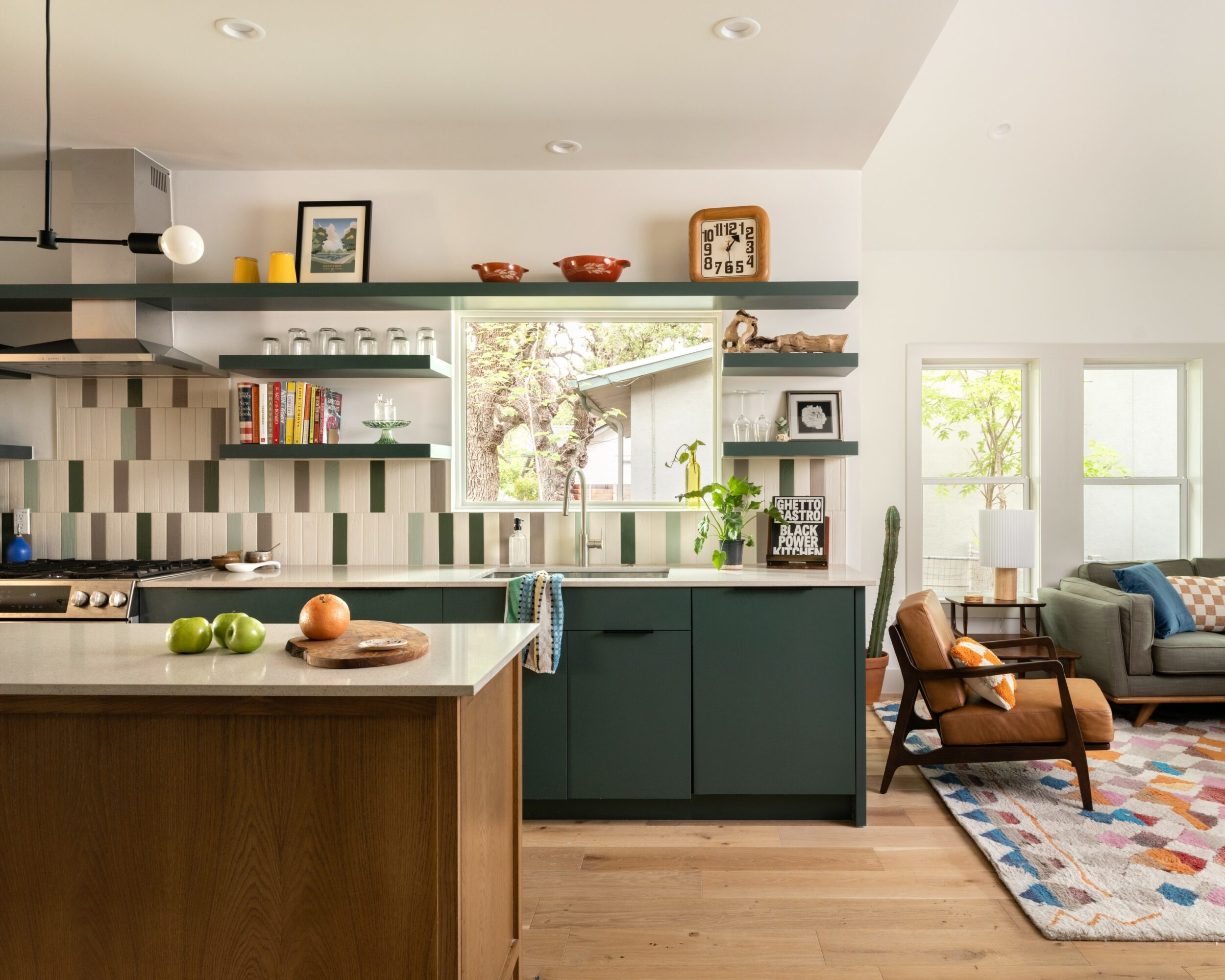 Kitchen with open shelves, window, and living room with sofa and armchair visible in the background.