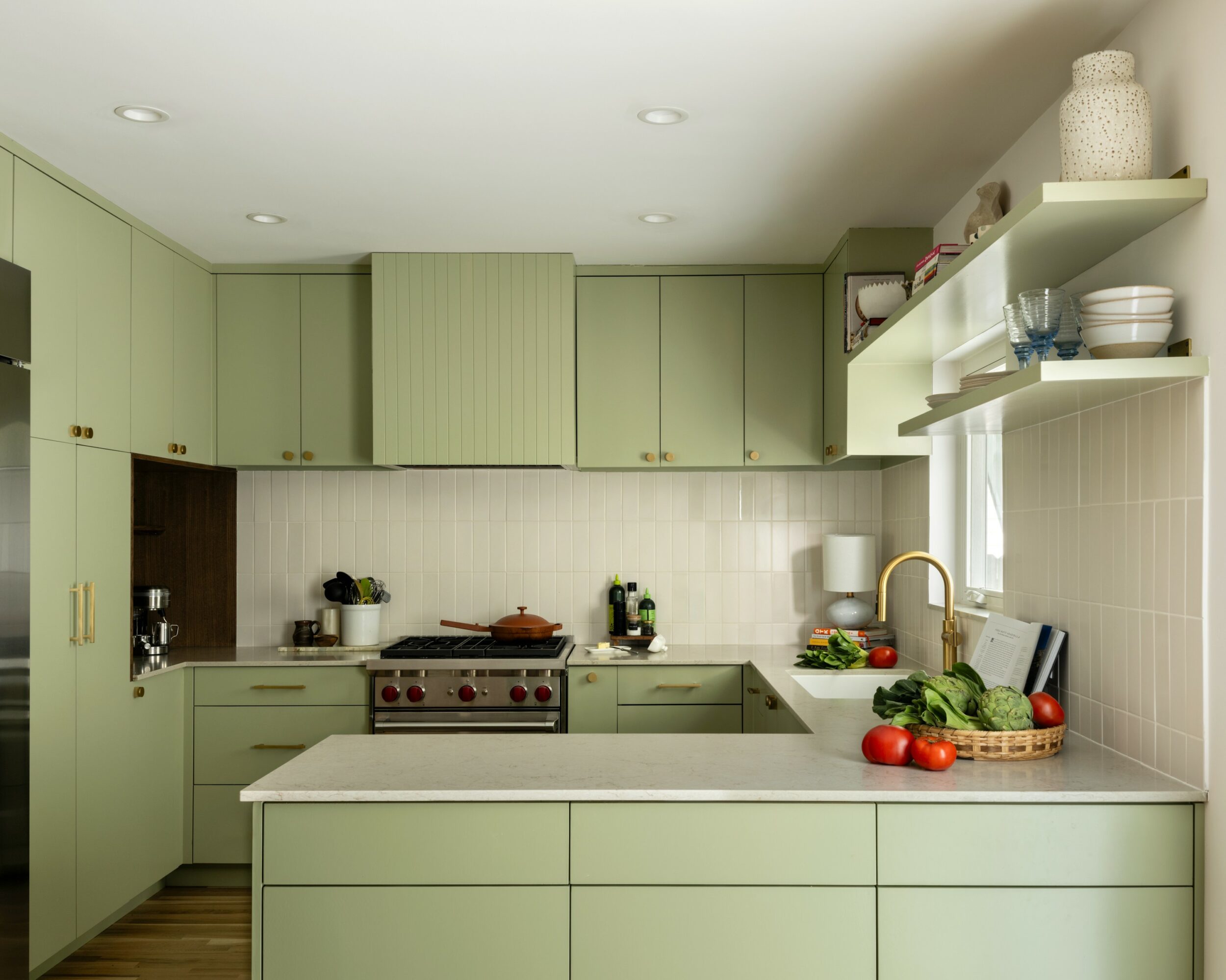 Kitchen with light green cabinets, white countertops, and a window above the sink, with various kitchen items and vegetables.