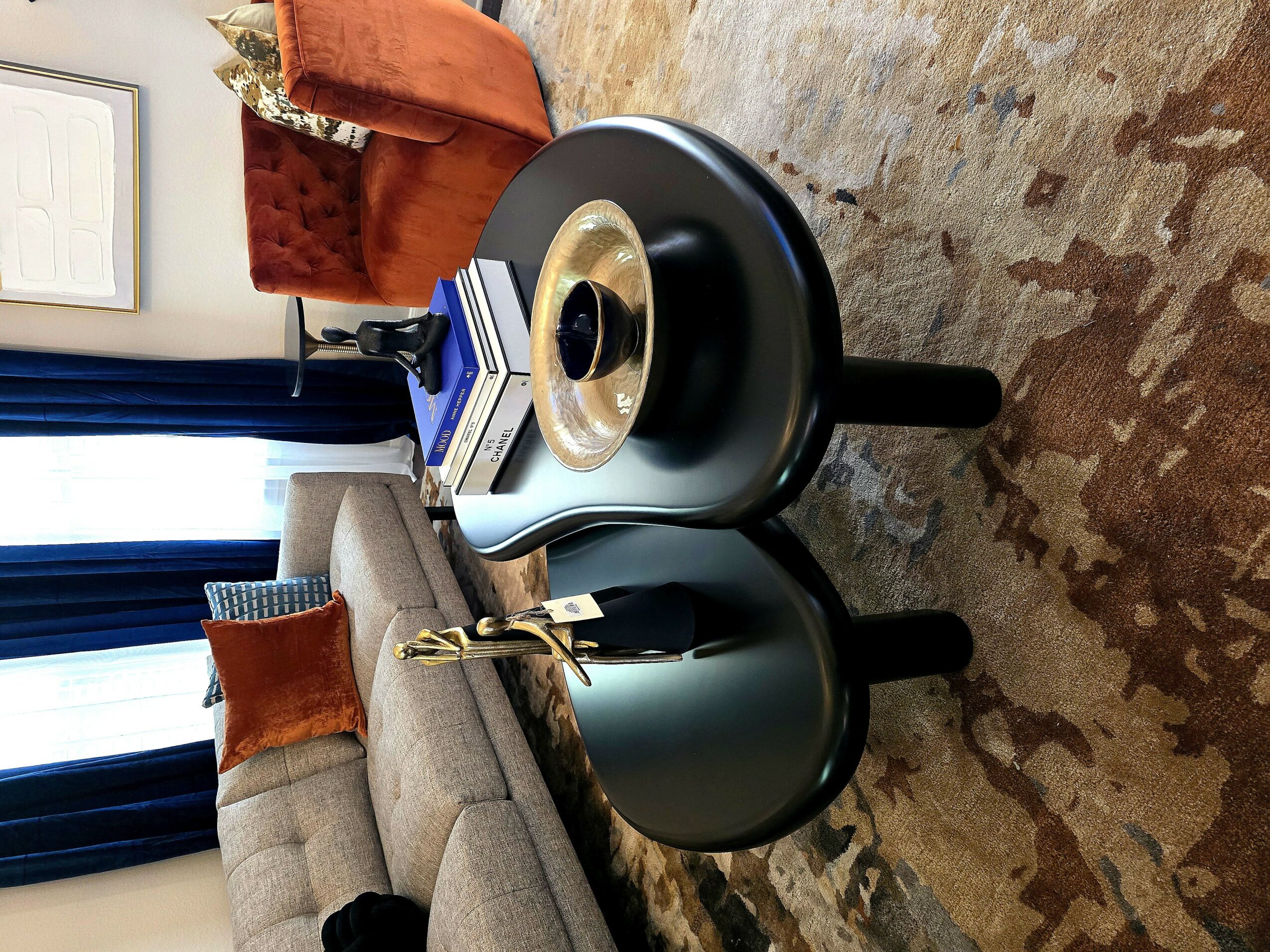 Living room with a gray sofa, orange armchair, and a round black coffee table on a patterned rug.
