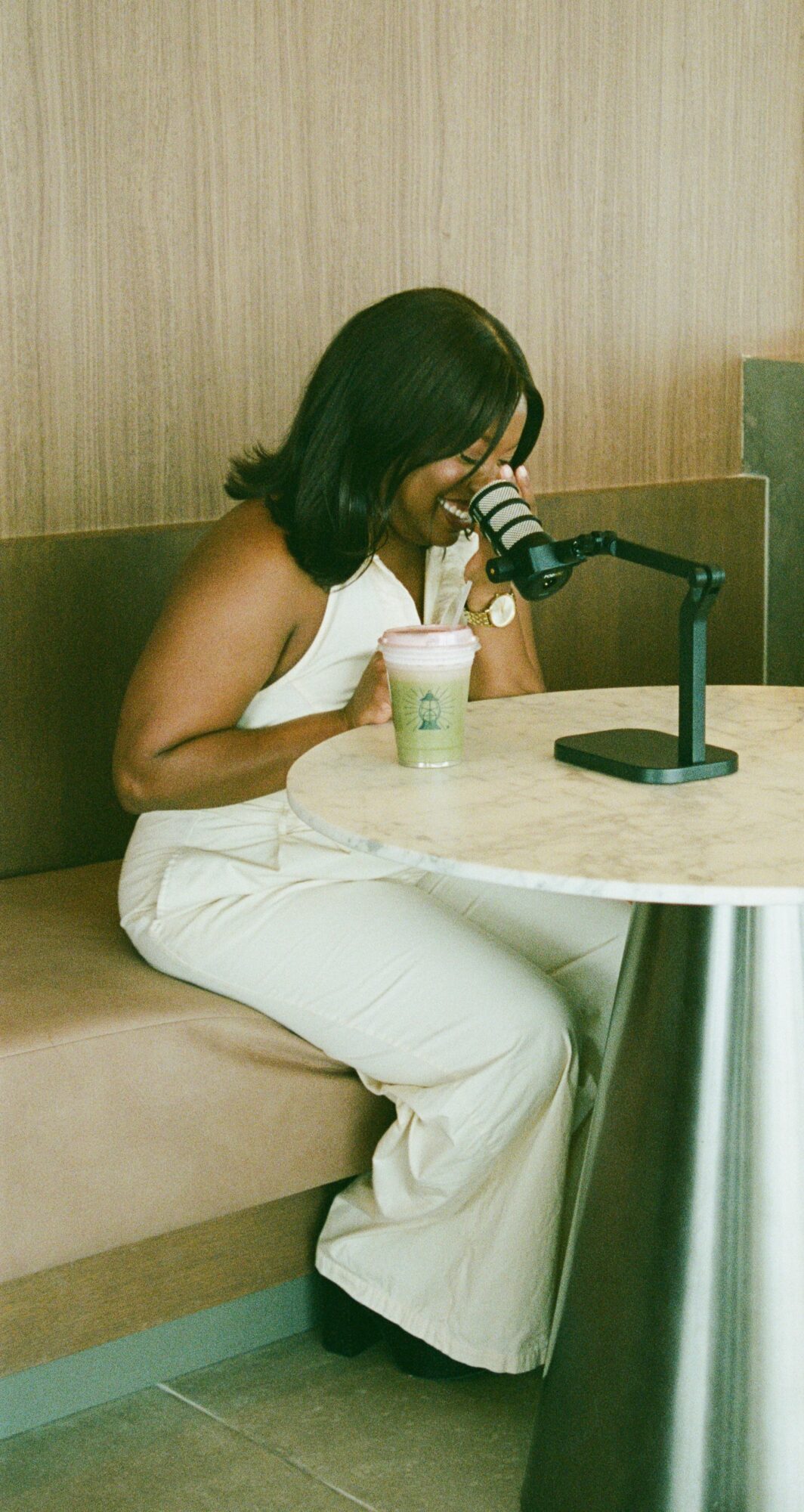Woman with dark hair in white outfit sitting at table, looking through a telescope, in a room with wood-paneled wall.
