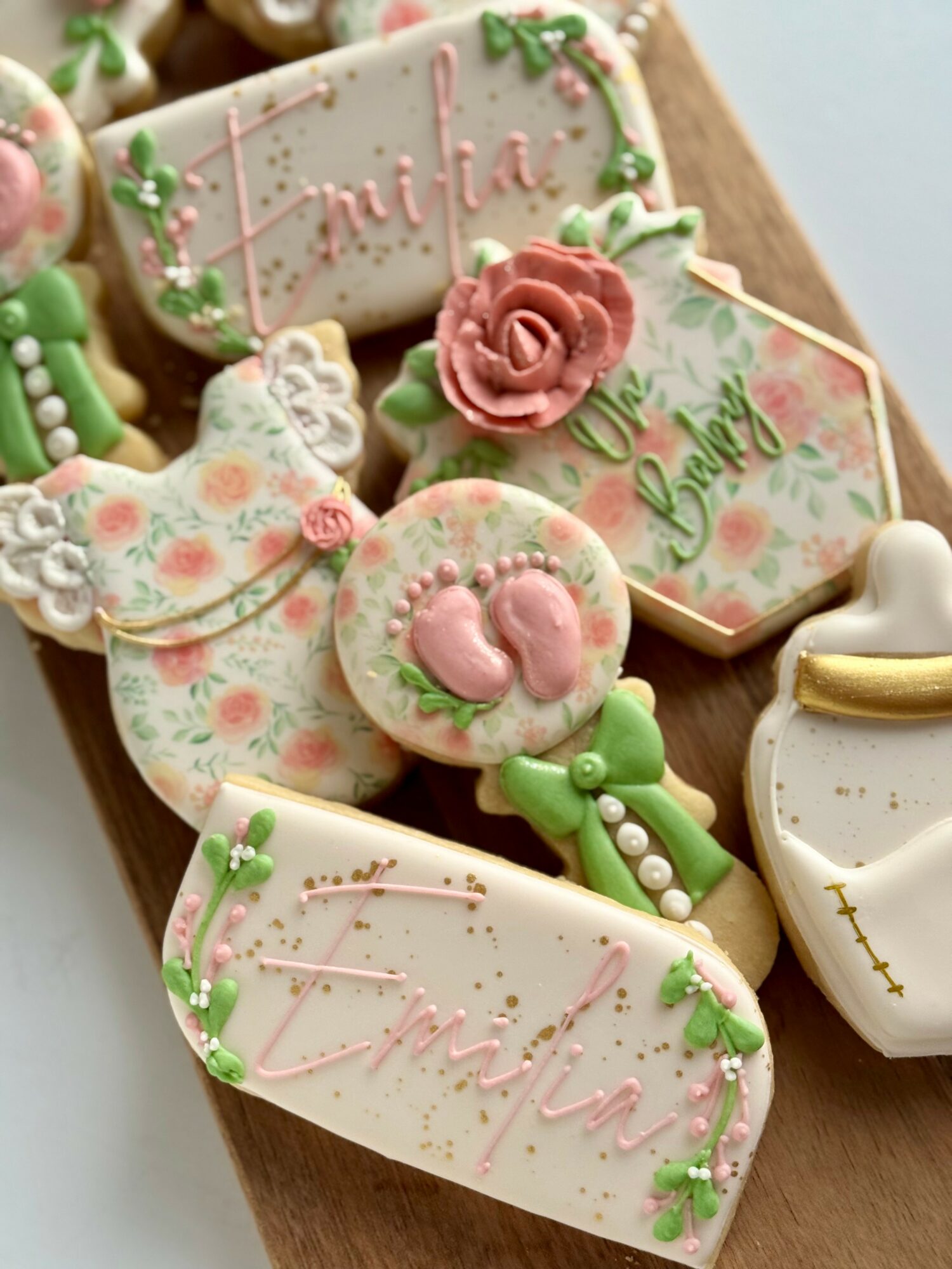 Decorative cookies with pink roses, green accents, and cursive pink writing, arranged on a wooden surface.
