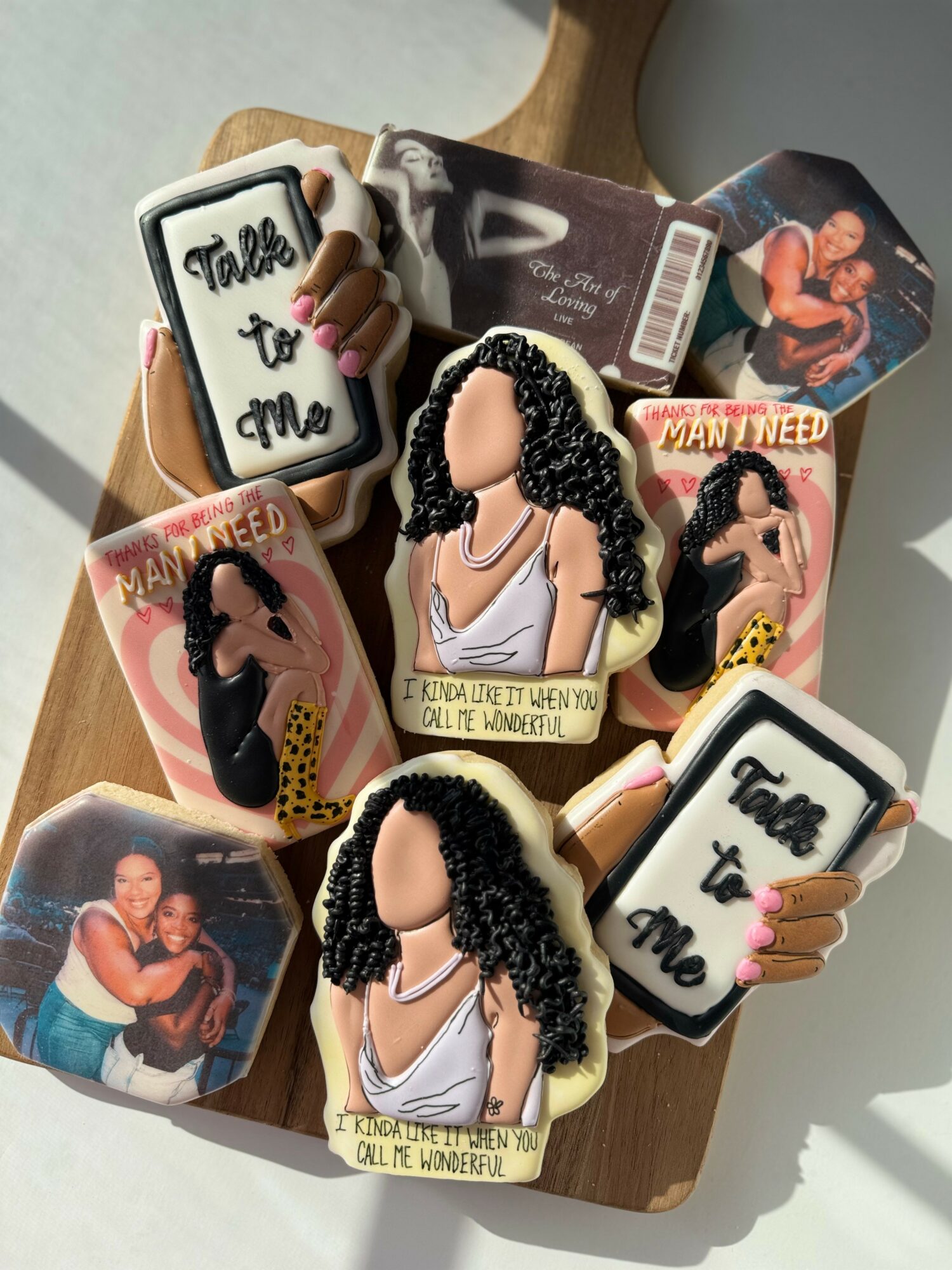 Collection of cookies and photo blocks on a wooden tray, featuring images of a woman with curly hair and text, with sunlight casting shadows.