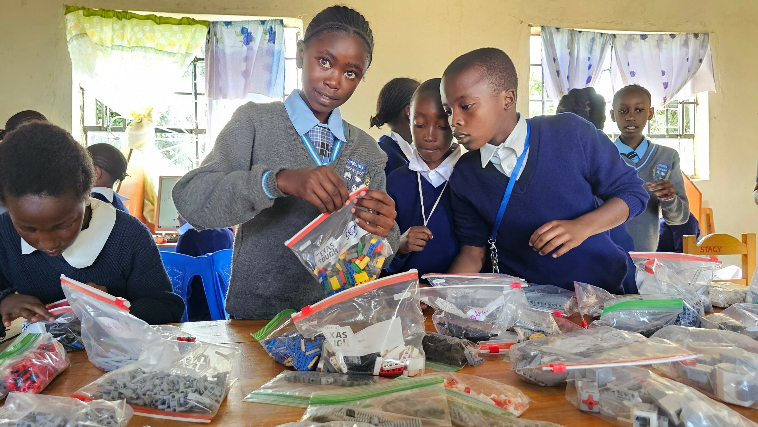 Group of children gathered around a table with plastic bags and craft supplies, engaging in an activity indoors.