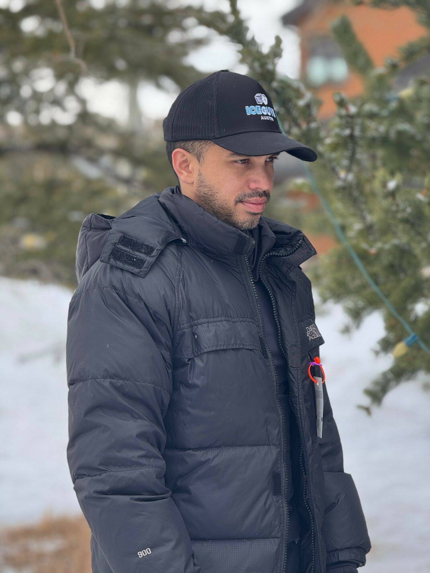 Man in black winter jacket and cap outdoors in snowy environment, looking to the side.