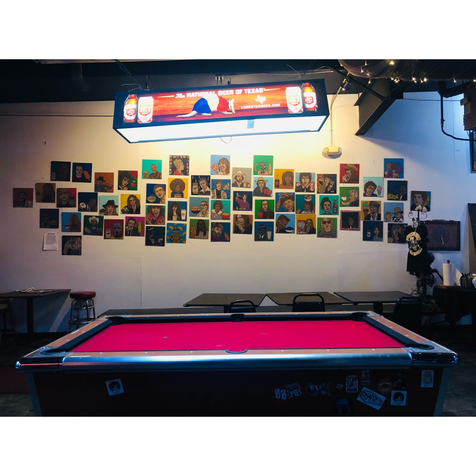 Pool table in a room with a wall display of colorful photographs, a digital sign, and a person standing nearby.