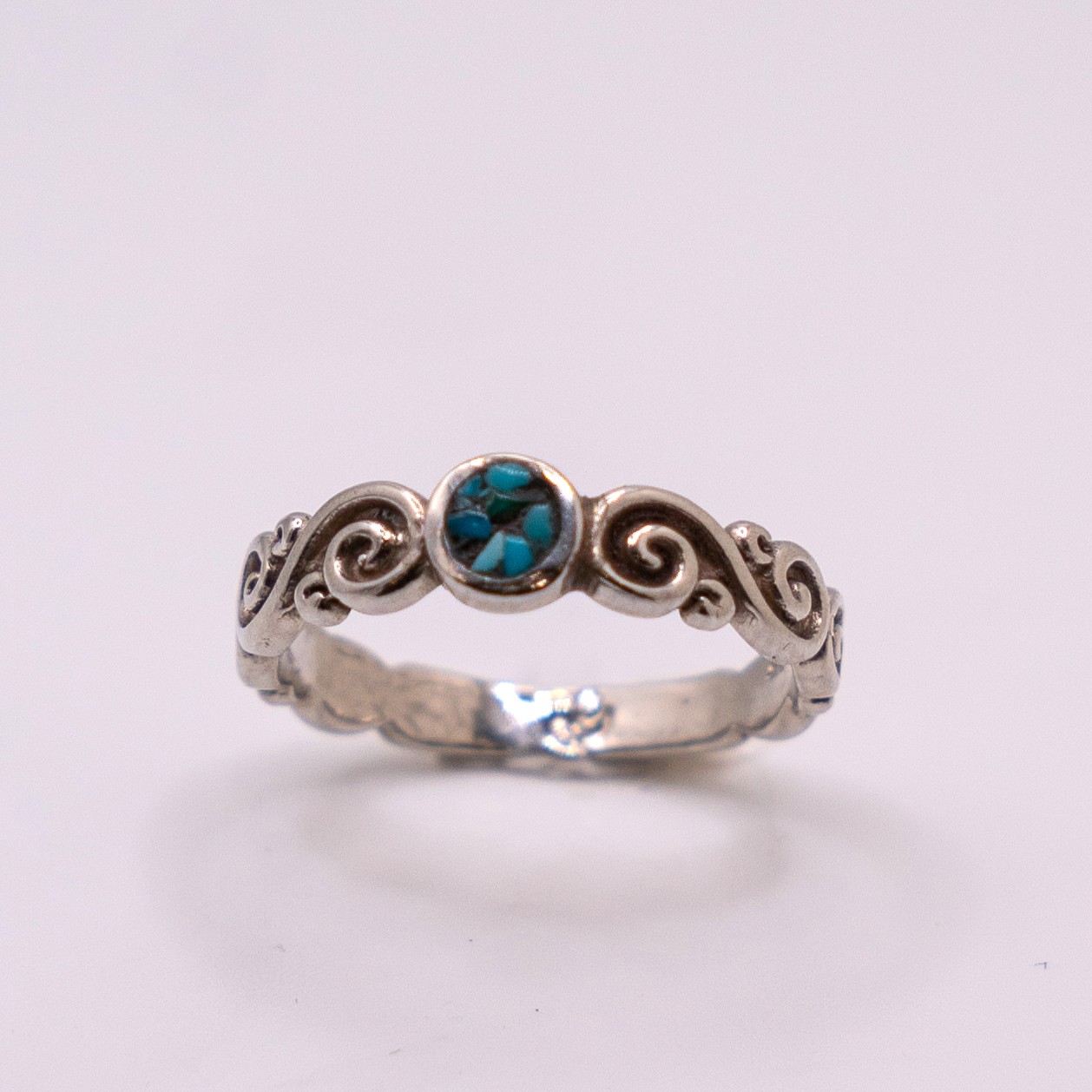Silver ring with a central turquoise stone and decorative swirls on a plain background.