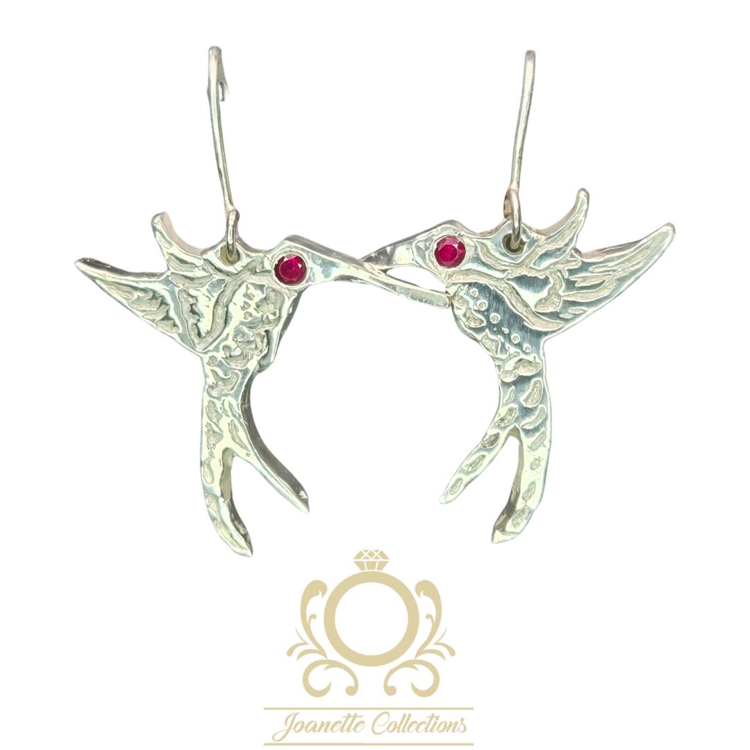 Pair of silver hummingbird earrings with pink gemstones, facing each other, with hooks at the top, on a white background.