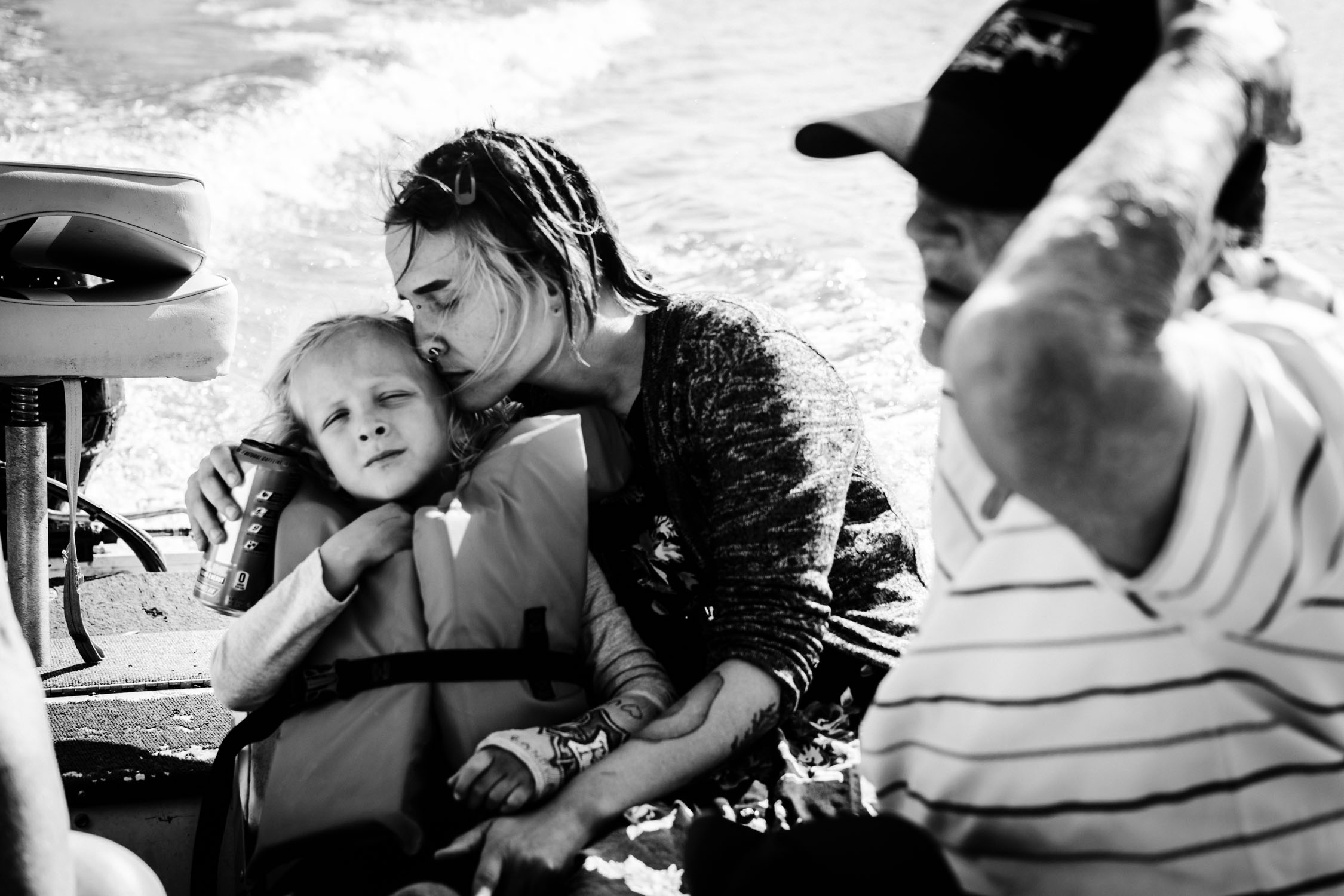 Woman comforting a child in a boat, with a man in a striped shirt nearby, in black and white.