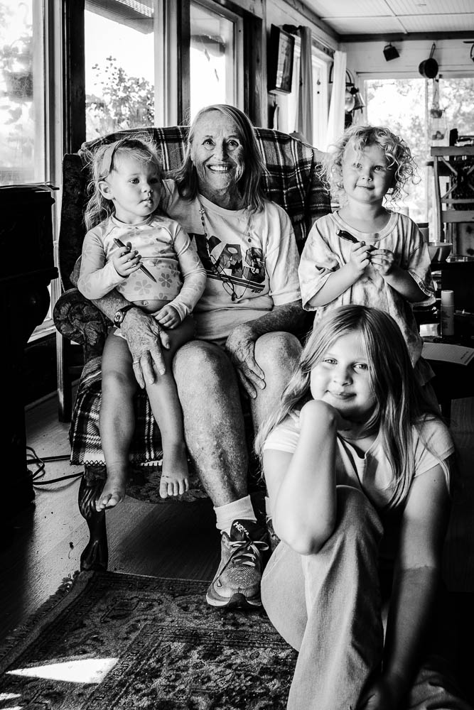 Woman with three children sitting indoors, two girls standing and one girl sitting in front, smiling and looking at the camera.