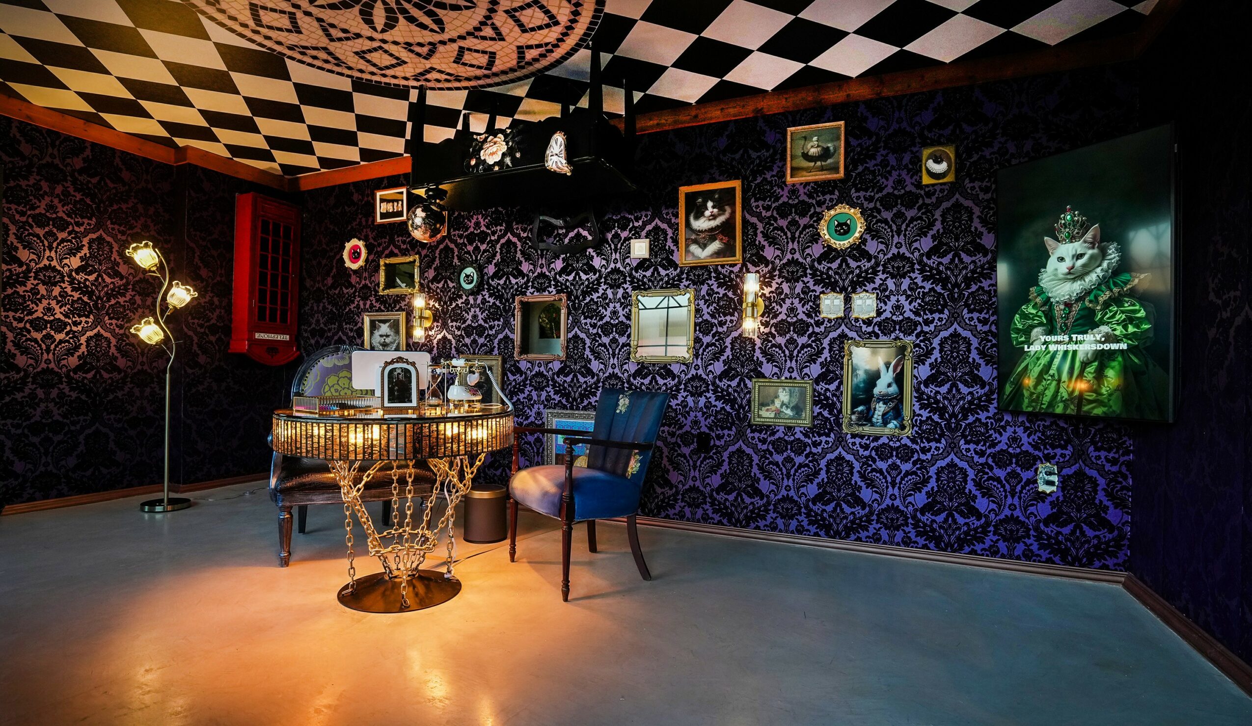 Room with a dark patterned wall, framed pictures, a piano, and a blue armchair, decorated with lights and artwork.