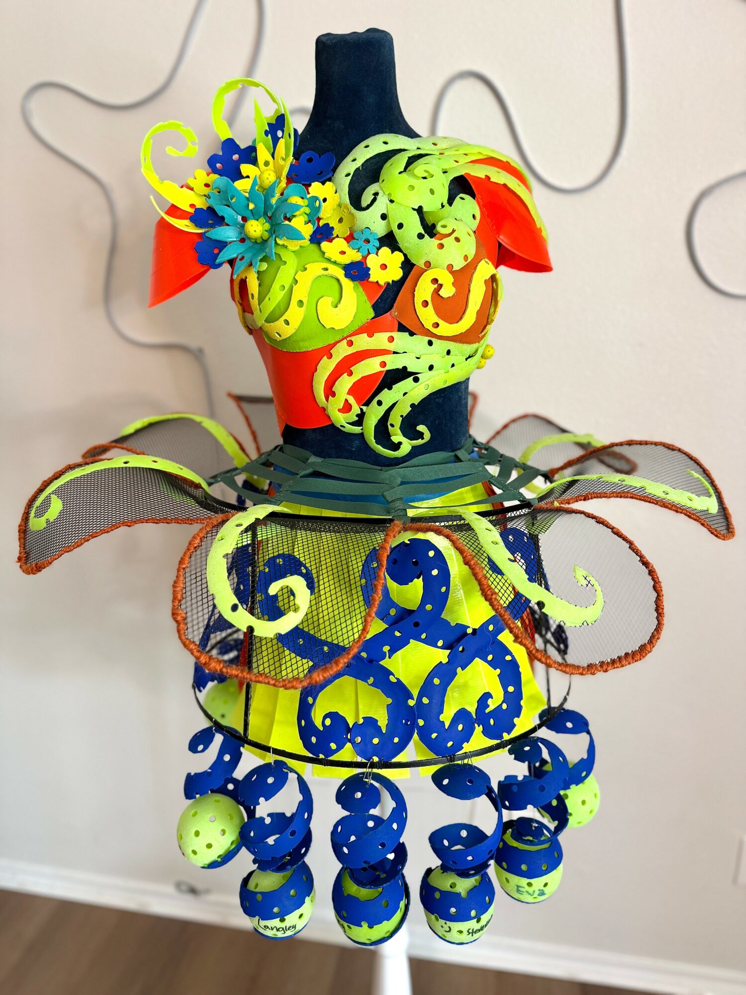 Colorful, layered costume with bright patterns, ruffles, and hanging ornaments, resembling a festive or theatrical outfit.