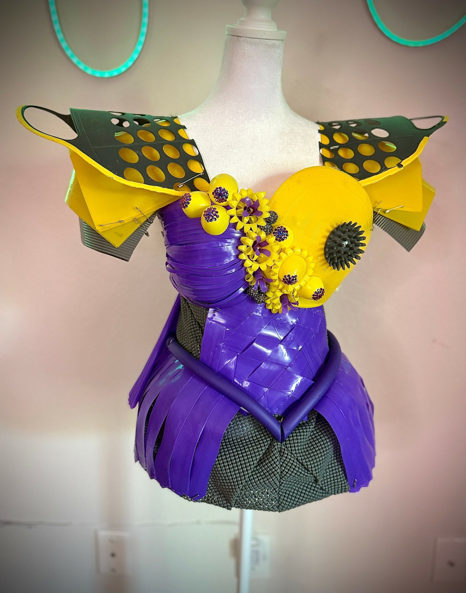 Colorful fashion piece with yellow, purple, and black elements on a mannequin, featuring large circular shapes and layered materials.
