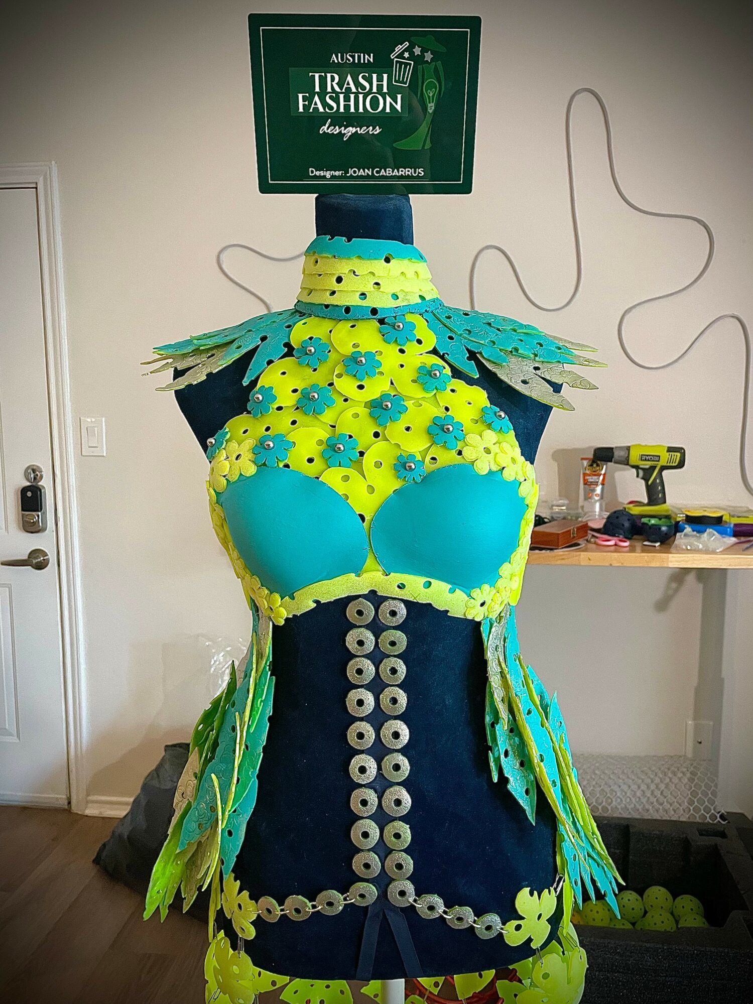 Dress form wearing a colorful, floral-themed costume with a sign reading 'Trash Fashion' above it.