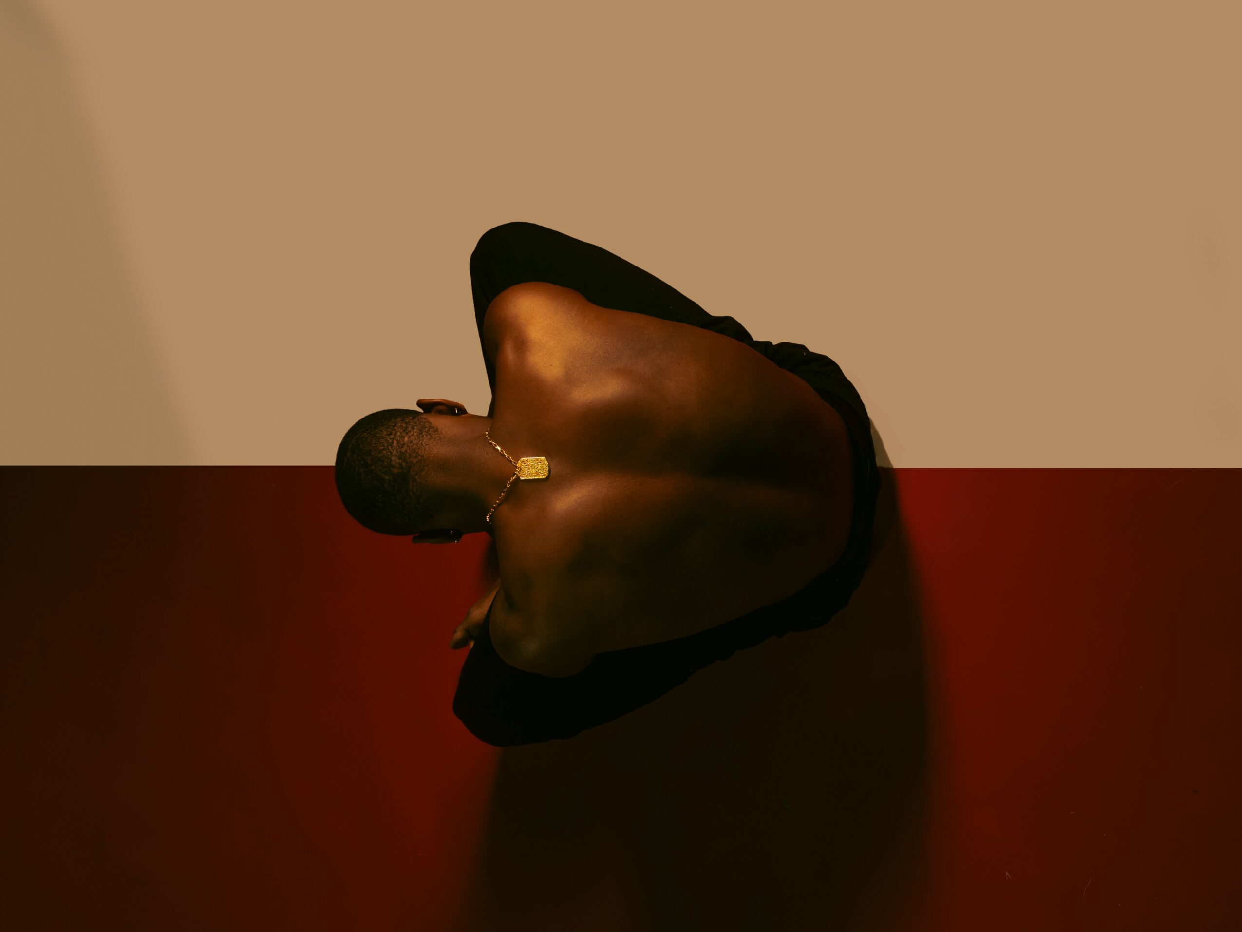 Person sitting with head down, arms wrapped around knees, on a two-tone floor and wall background.