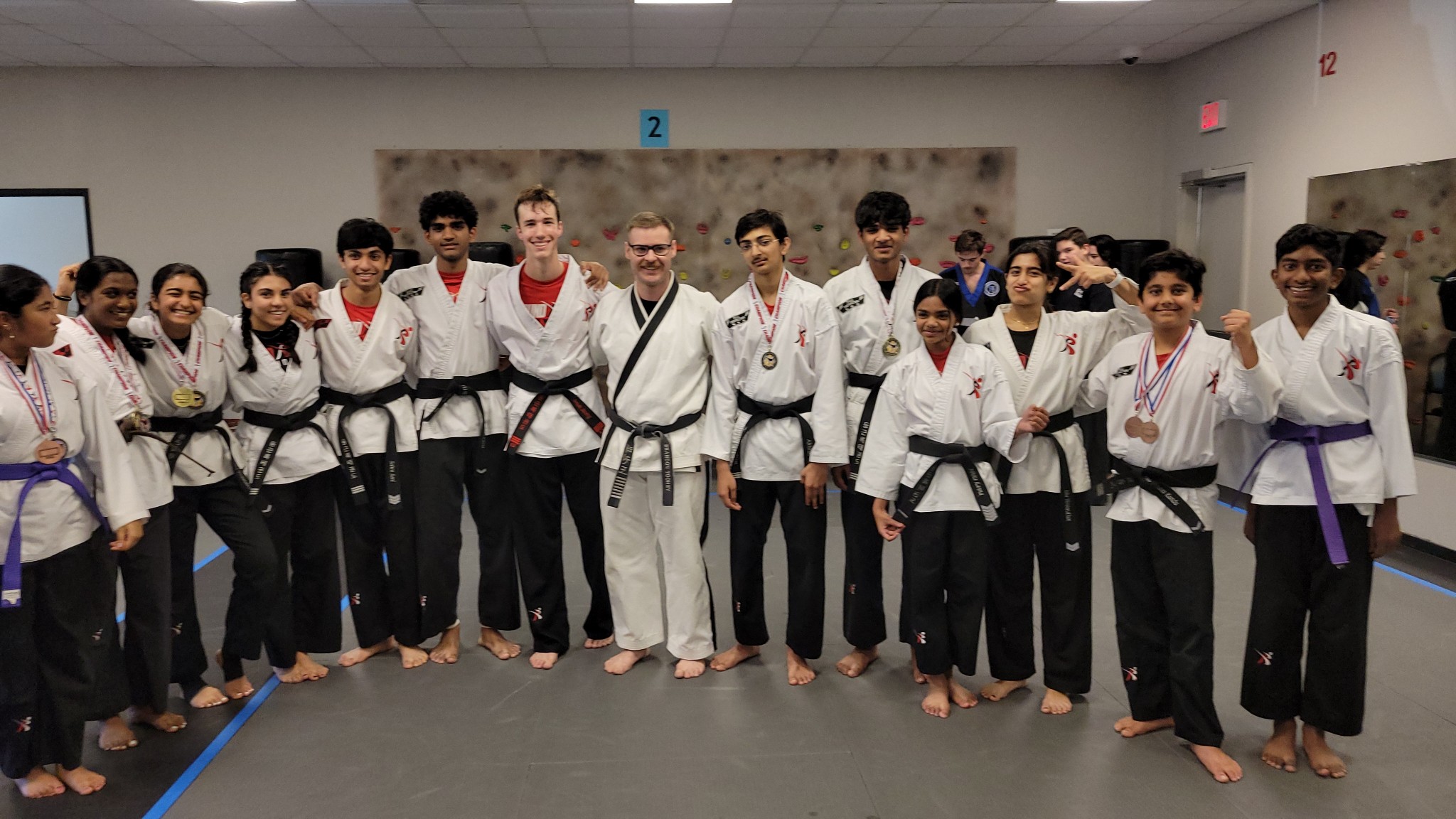 Group of people in martial arts uniforms standing in a dojo, smiling for a photo.