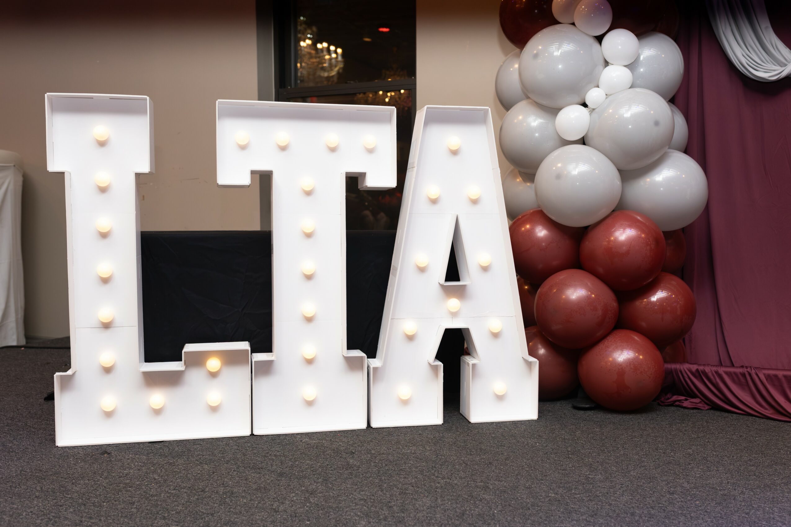 Large illuminated letters spelling 'LTA' with balloons in the background, on a dark surface.