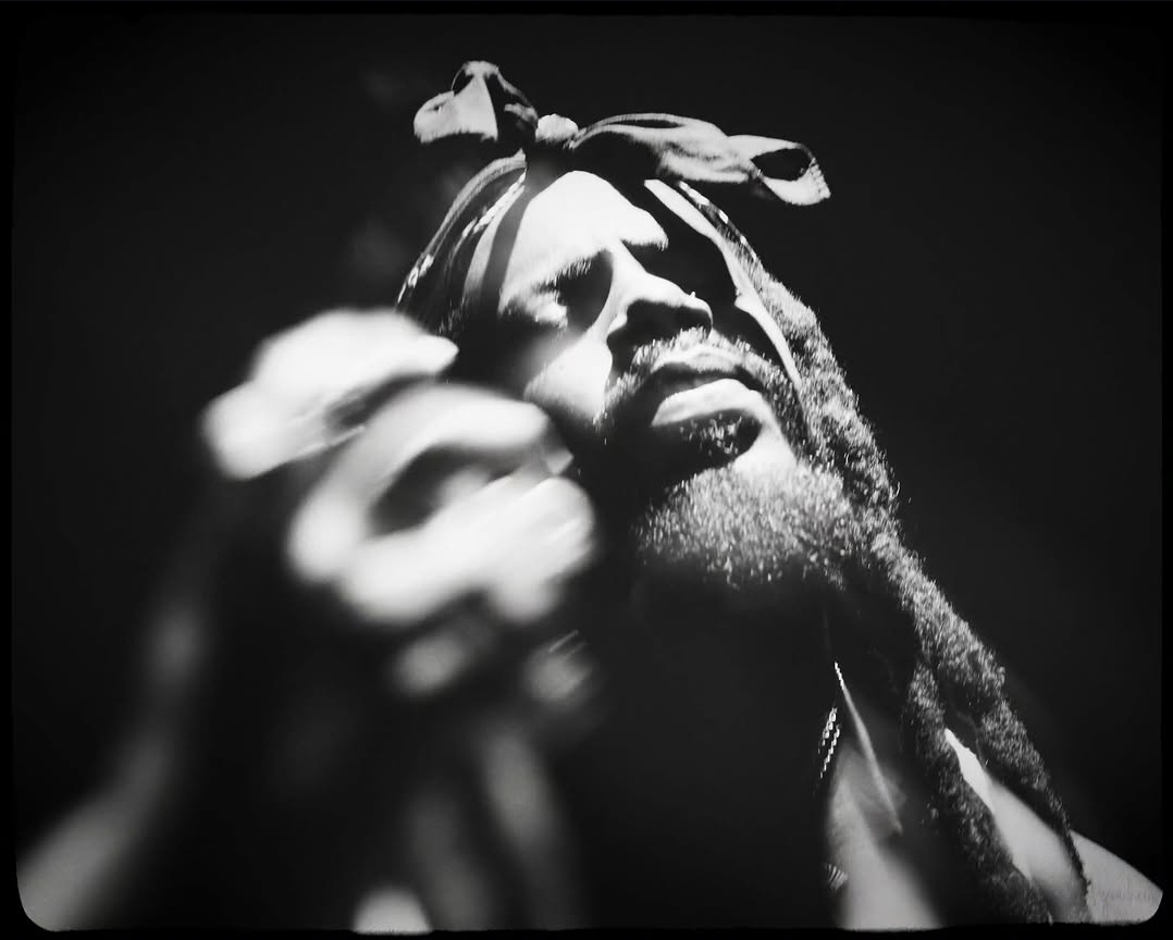 Person with dreadlocks holding an object, face close-up, black and white image, expressive expression.