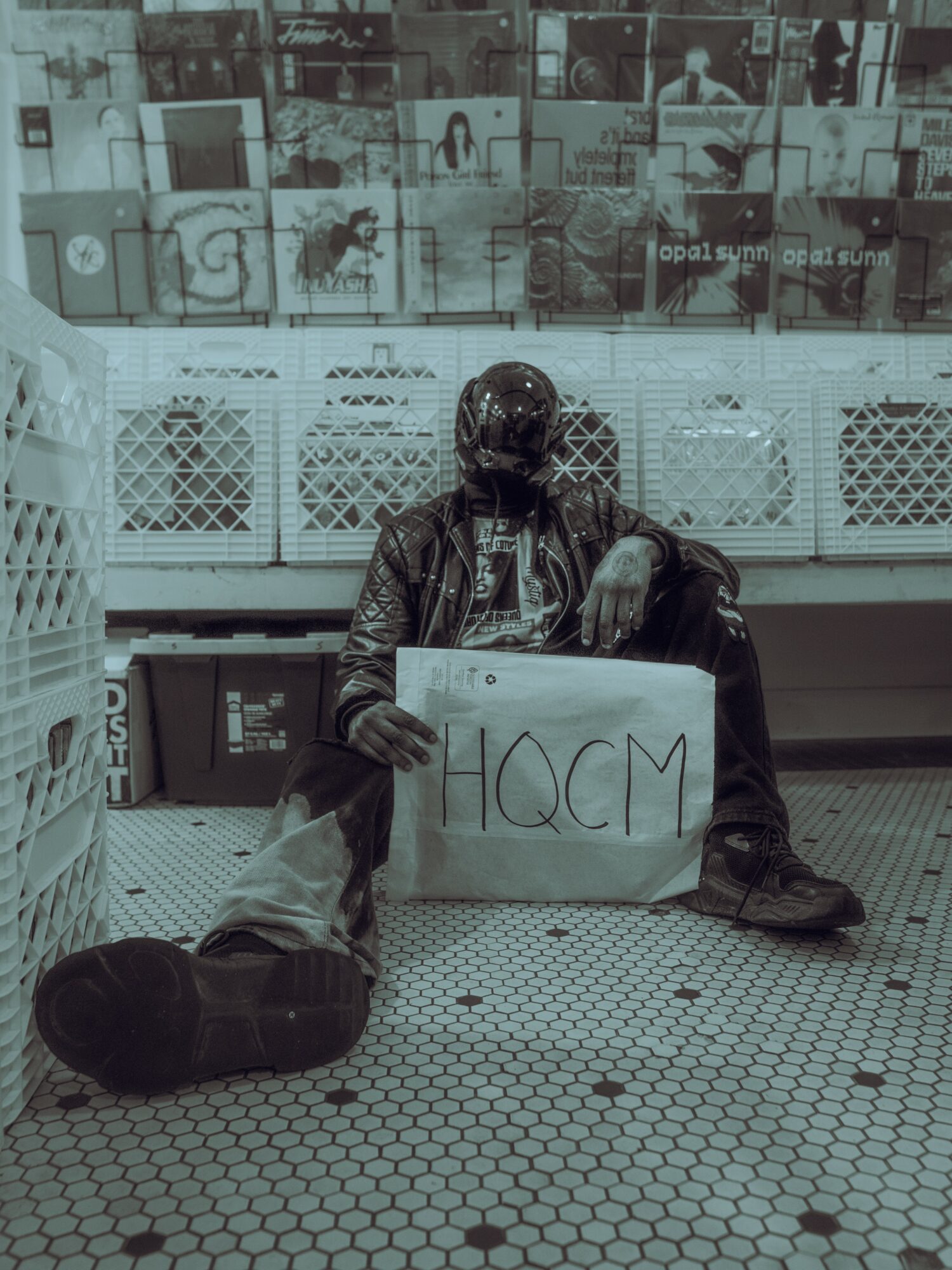 Person sitting on the floor holding a sign with the word 'HACM' in a public space, with a display of images above.