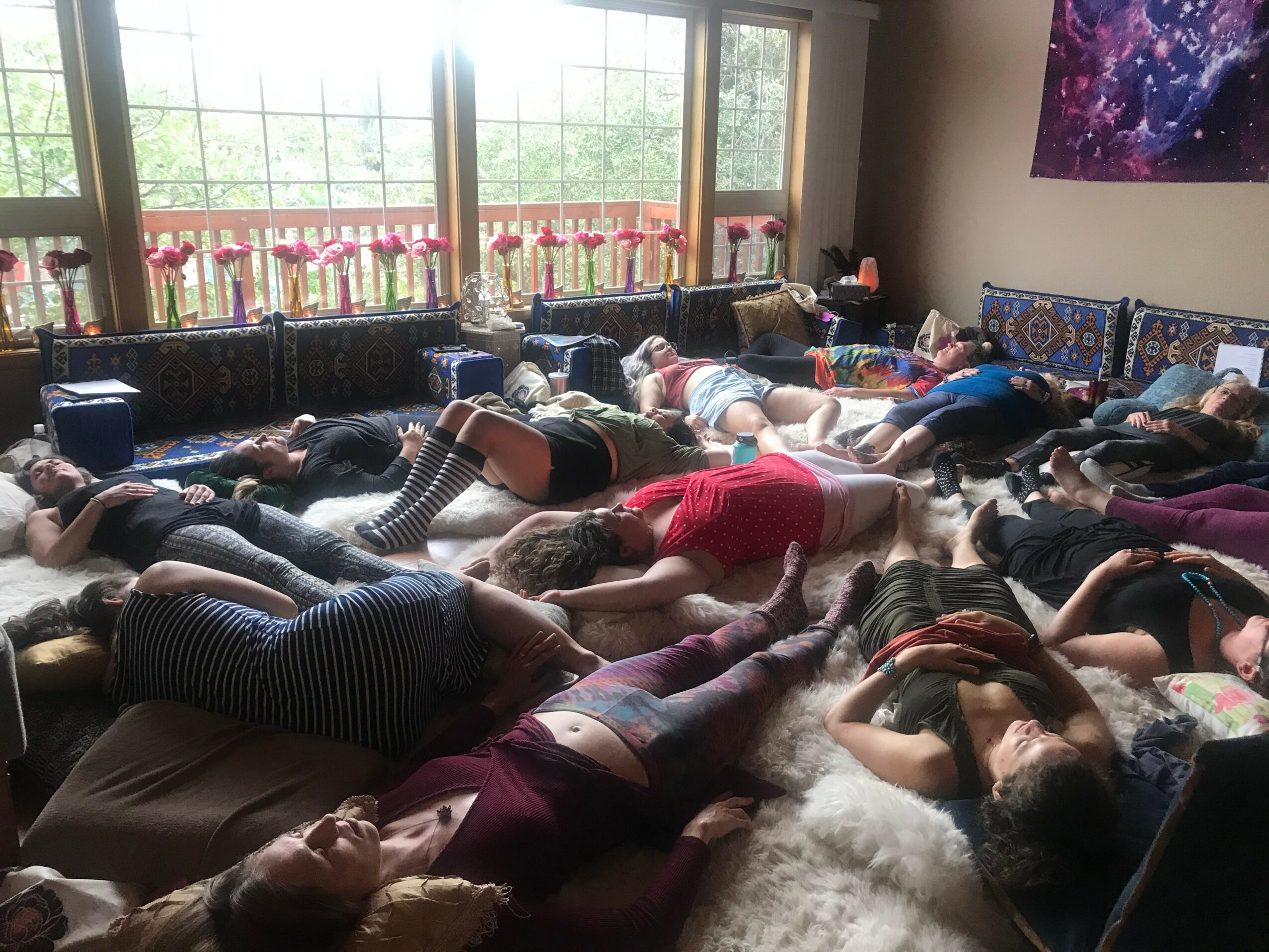 Group of people lying on the floor in a room with large windows and colorful decorations, resting or sleeping.