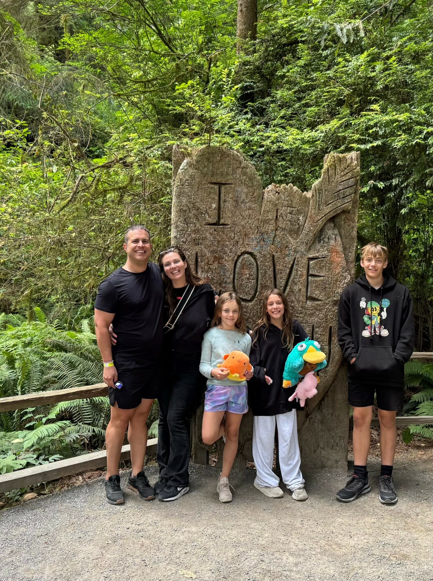 Five people stand in front of a large rock with the word 'LOVE' carved into it, surrounded by greenery.
