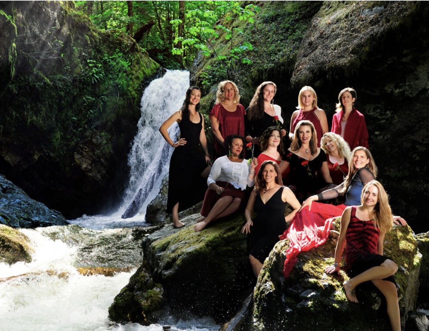 Group of women sitting and standing on rocks near a waterfall in a forested area.