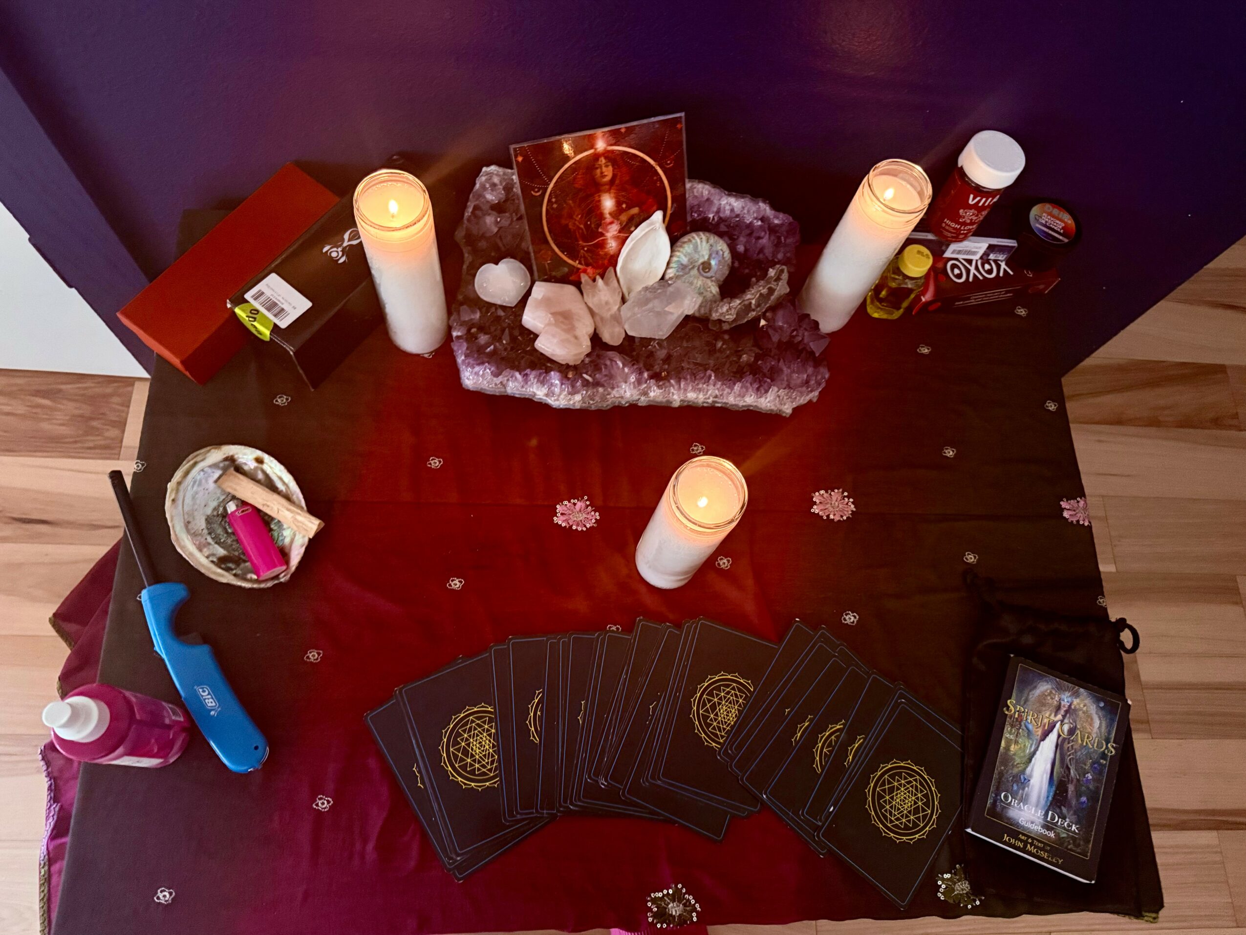 Table with candles, crystals, tarot cards, and bottles, arranged for a spiritual or ritual setting.