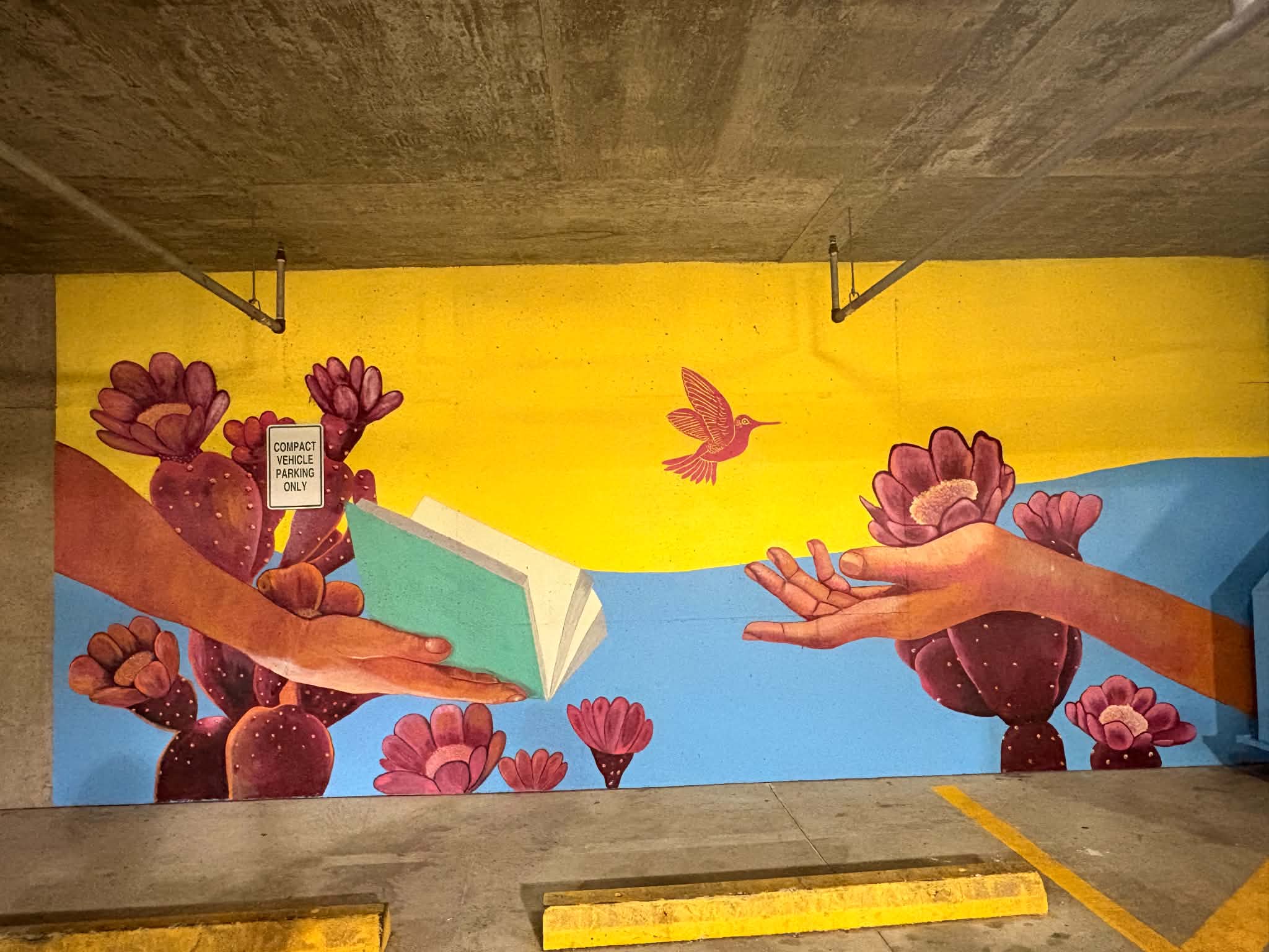 Colorful mural with flowers, a bird, and a hand reaching out against a yellow and blue background.