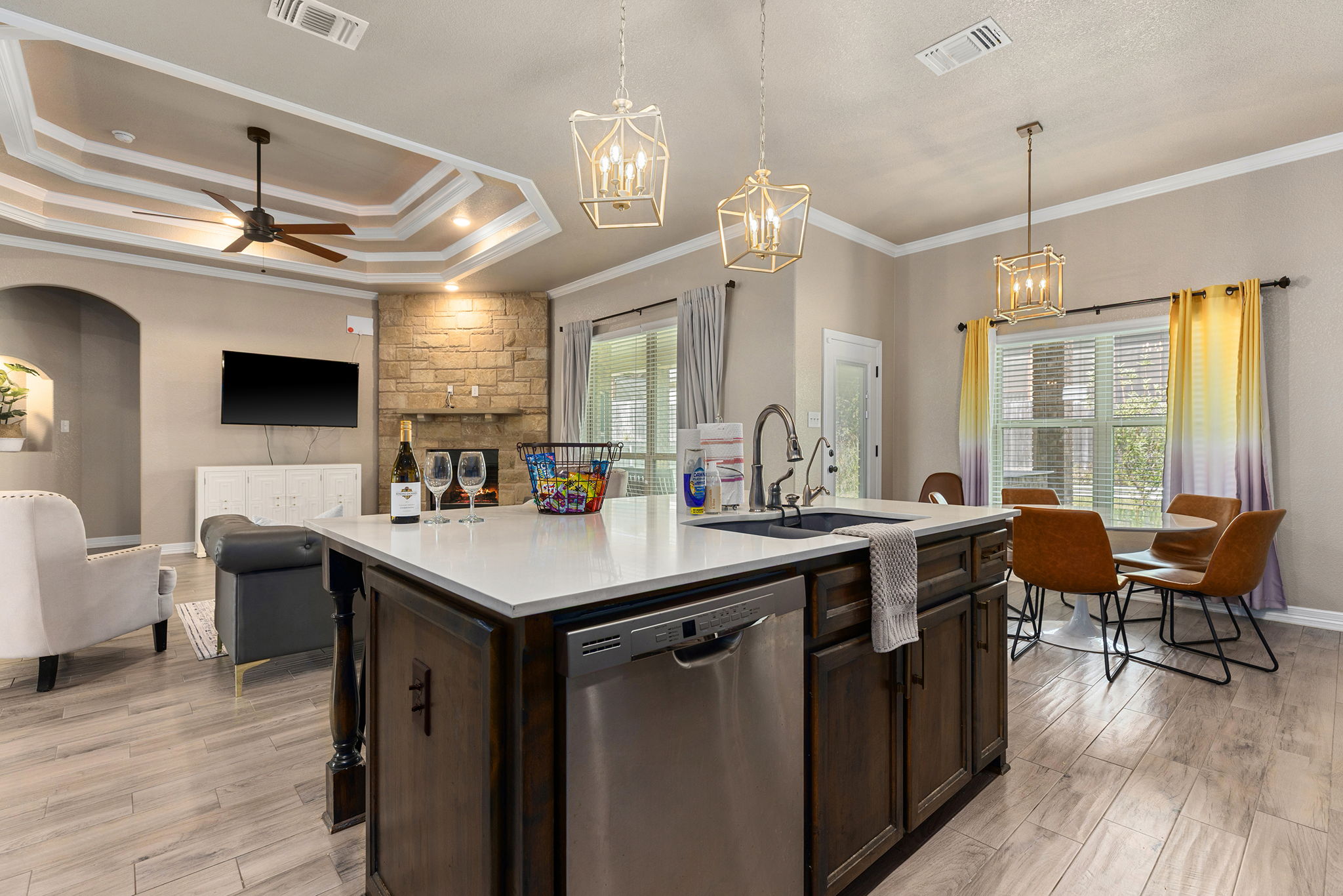 Open-concept living and dining area with a kitchen island, seating, and large windows with yellow curtains.