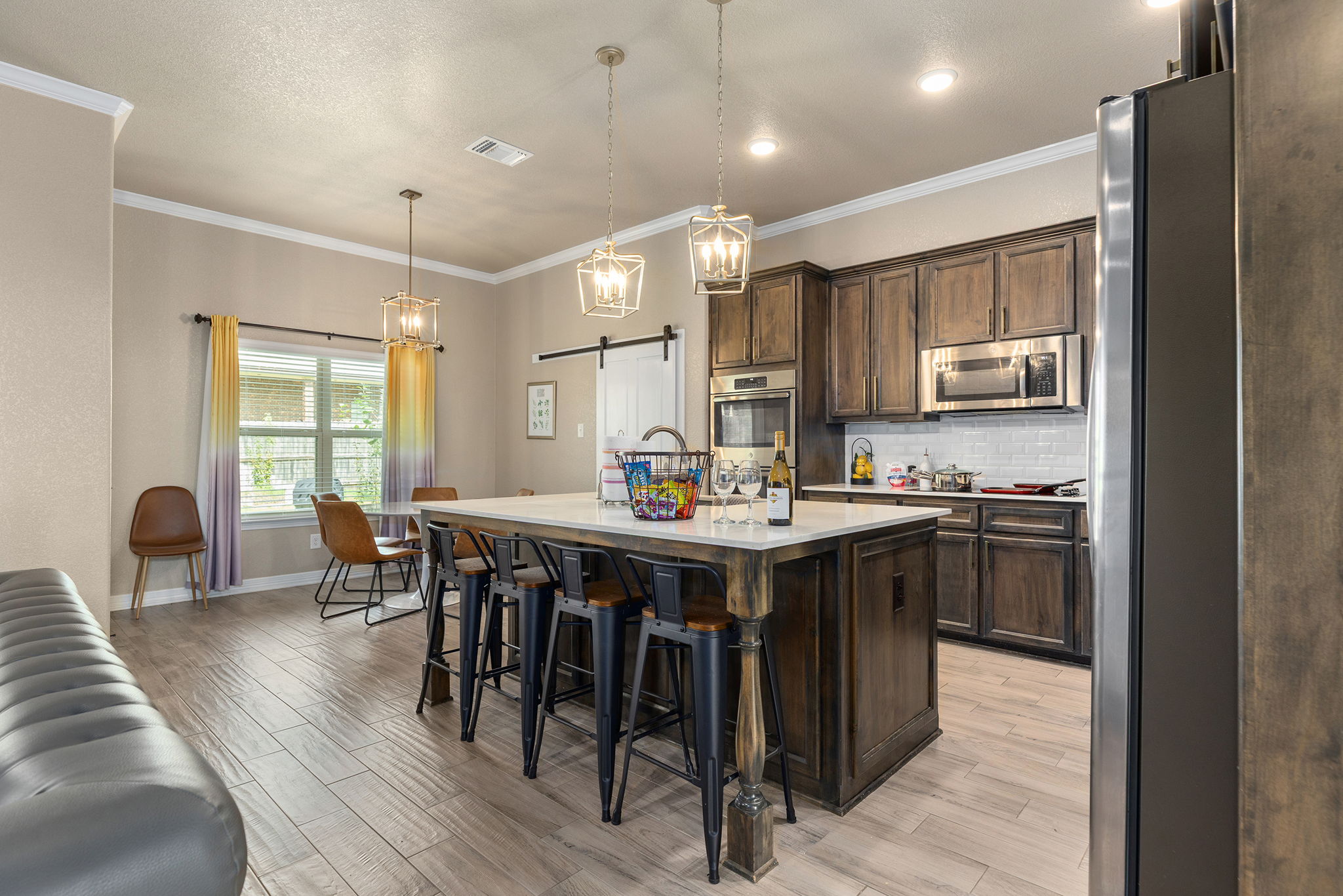Kitchen with island, dark wood cabinets, stainless steel appliances, and a dining area with chairs and windows.