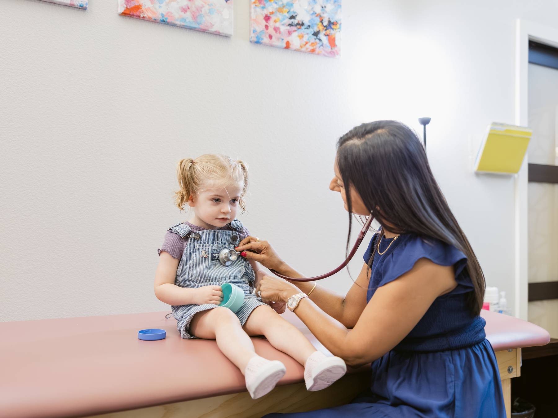 A healthcare professional examines a young girl sitting on an examination table in a clinic room.