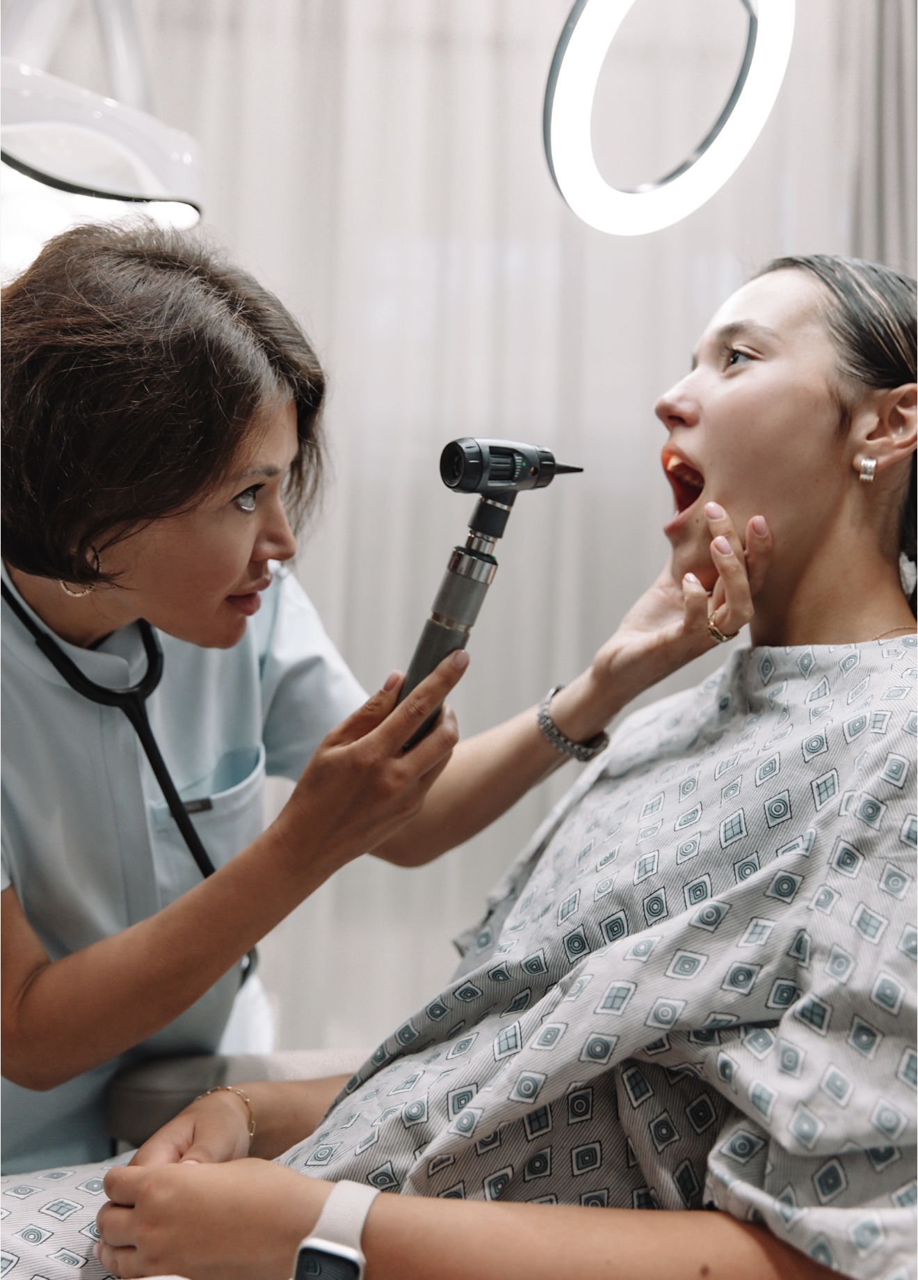 Doctor examines a young woman's throat with a lighted instrument in a clinical setting.