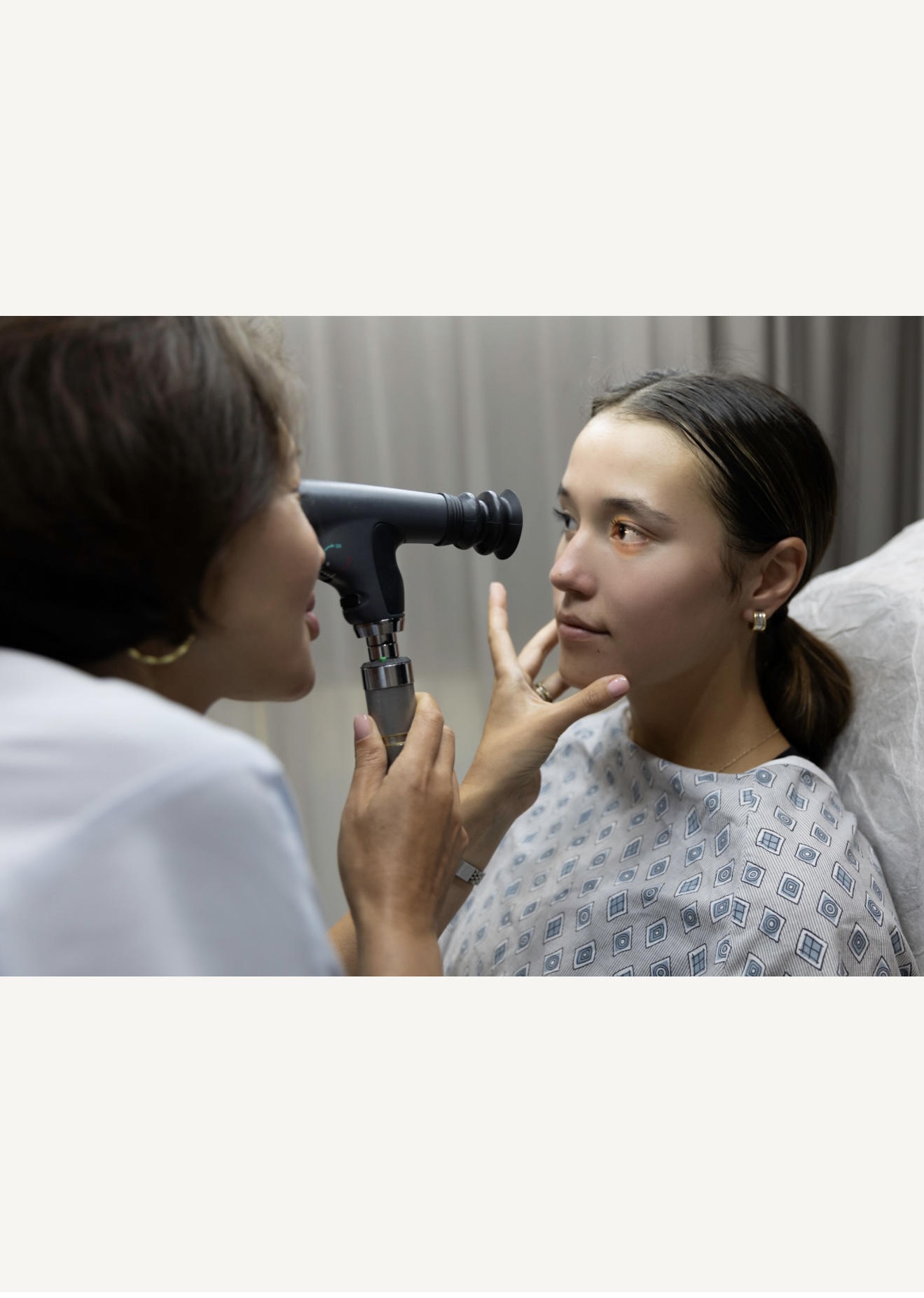 Doctor examines woman's eye with a handheld device in a clinical setting.