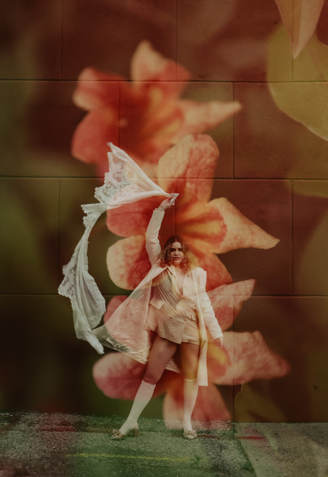 Person dressed as a fairy with wings and a wand, standing in front of a large flower background.