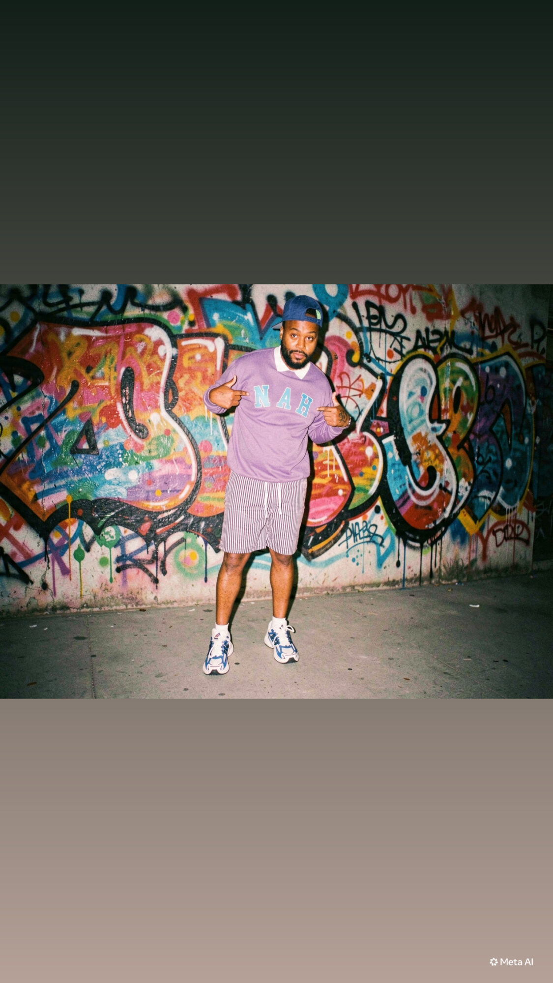 Man standing in front of a colorful graffiti wall, wearing a purple shirt, shorts, and sneakers.