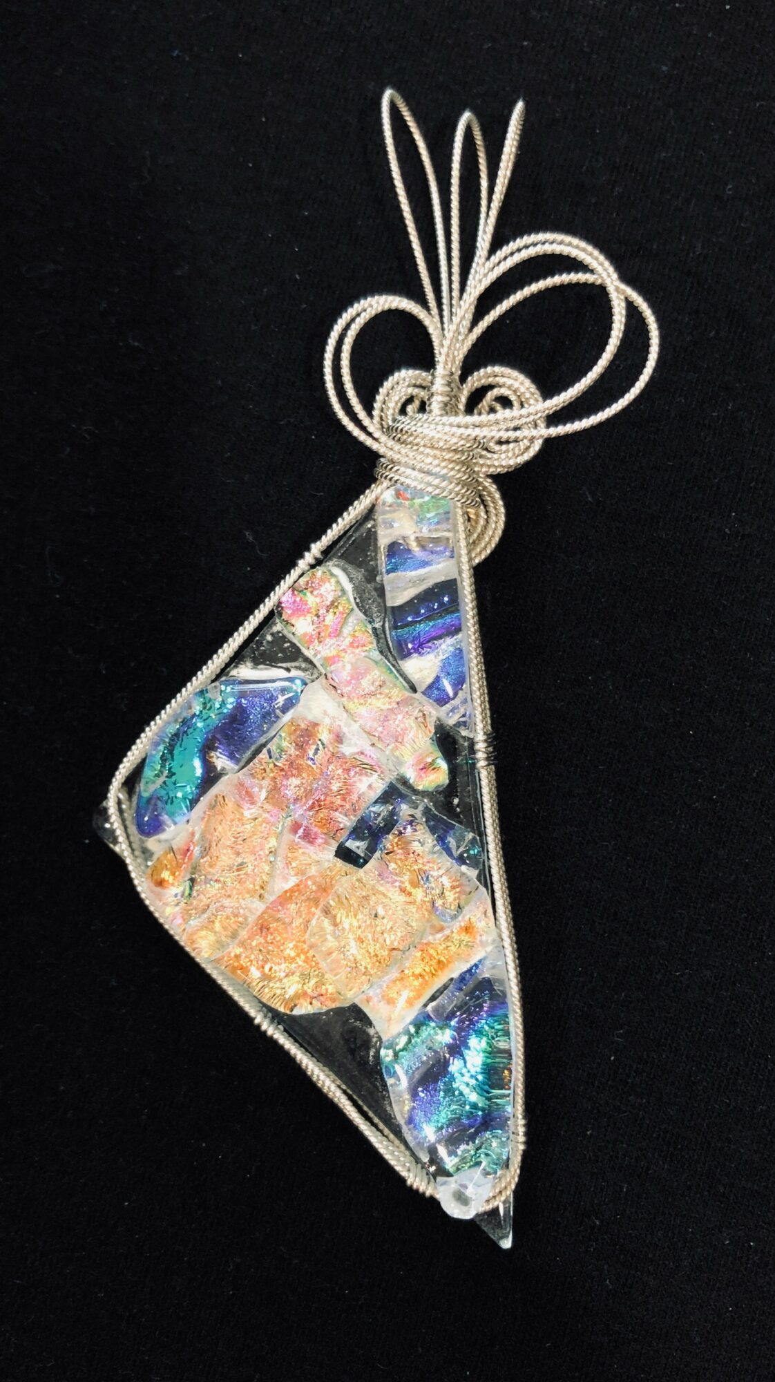 Decorative pendant with iridescent and glittery elements, hanging from a white string loop, against a black background.