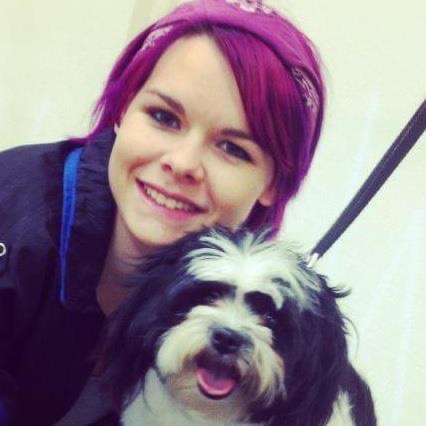 Young woman with pink hair smiling next to a small black and white dog with its tongue out.