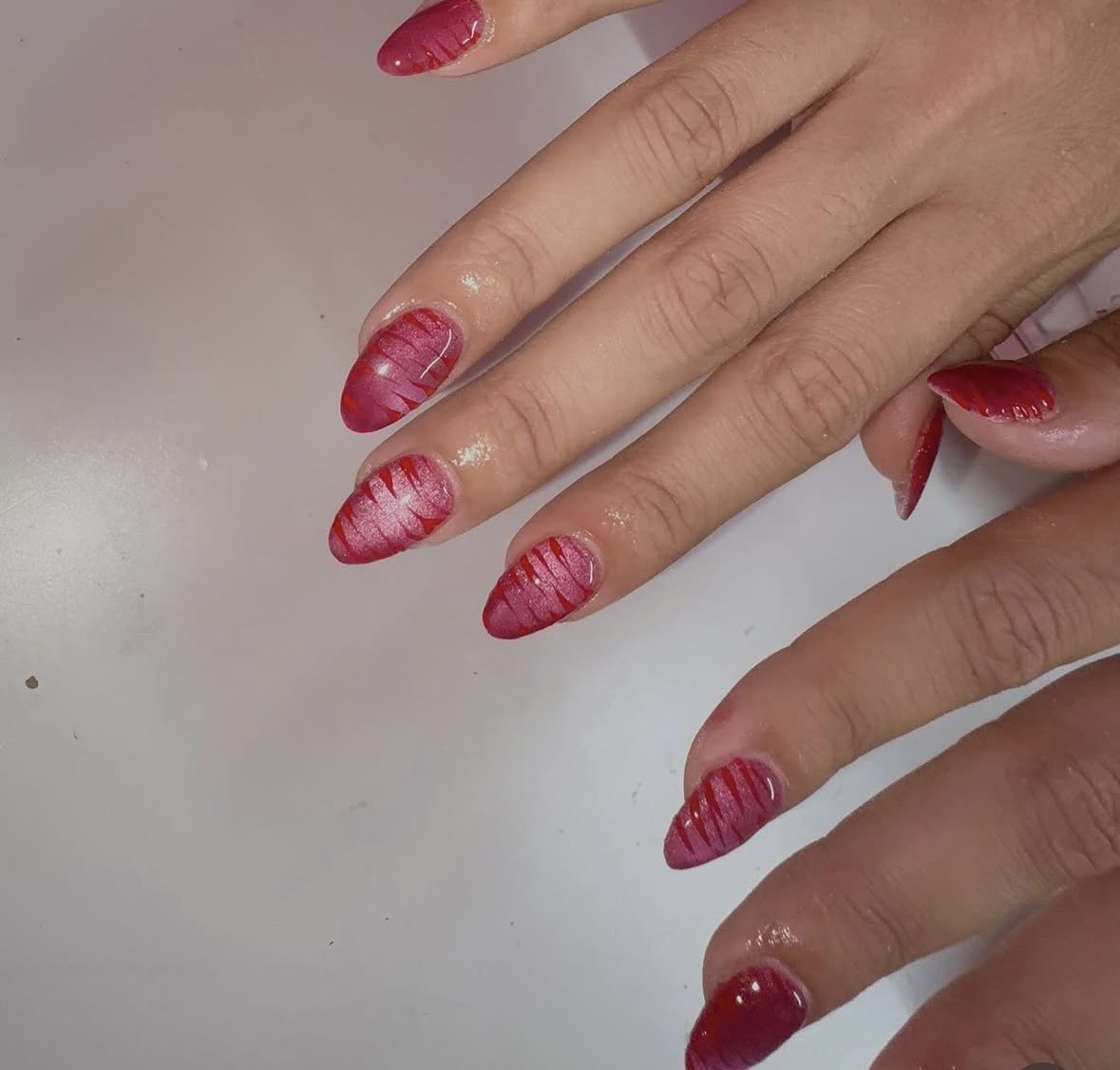 Hand with nails painted in pink and white striped design, resting on a light surface.