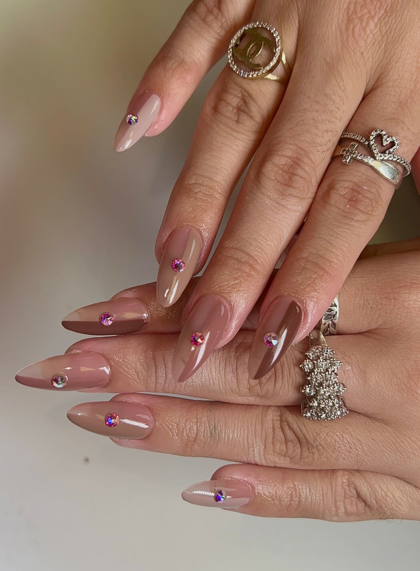 Close-up of hands with decorated nails and multiple rings, including a crown-shaped ring and a large floral ring.