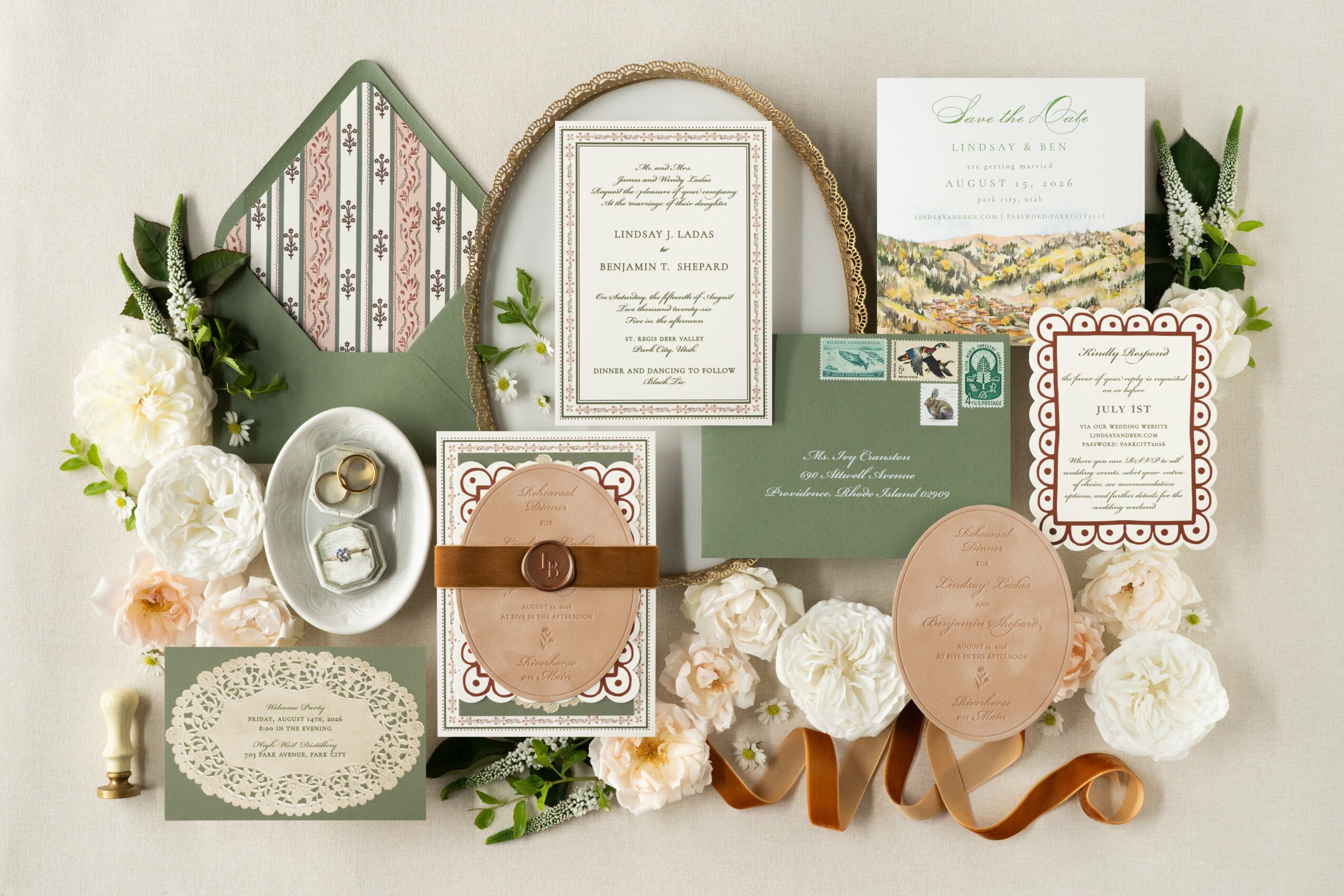 Wedding invitation, envelope, and decorative elements with flowers and greenery, arranged on a light background.