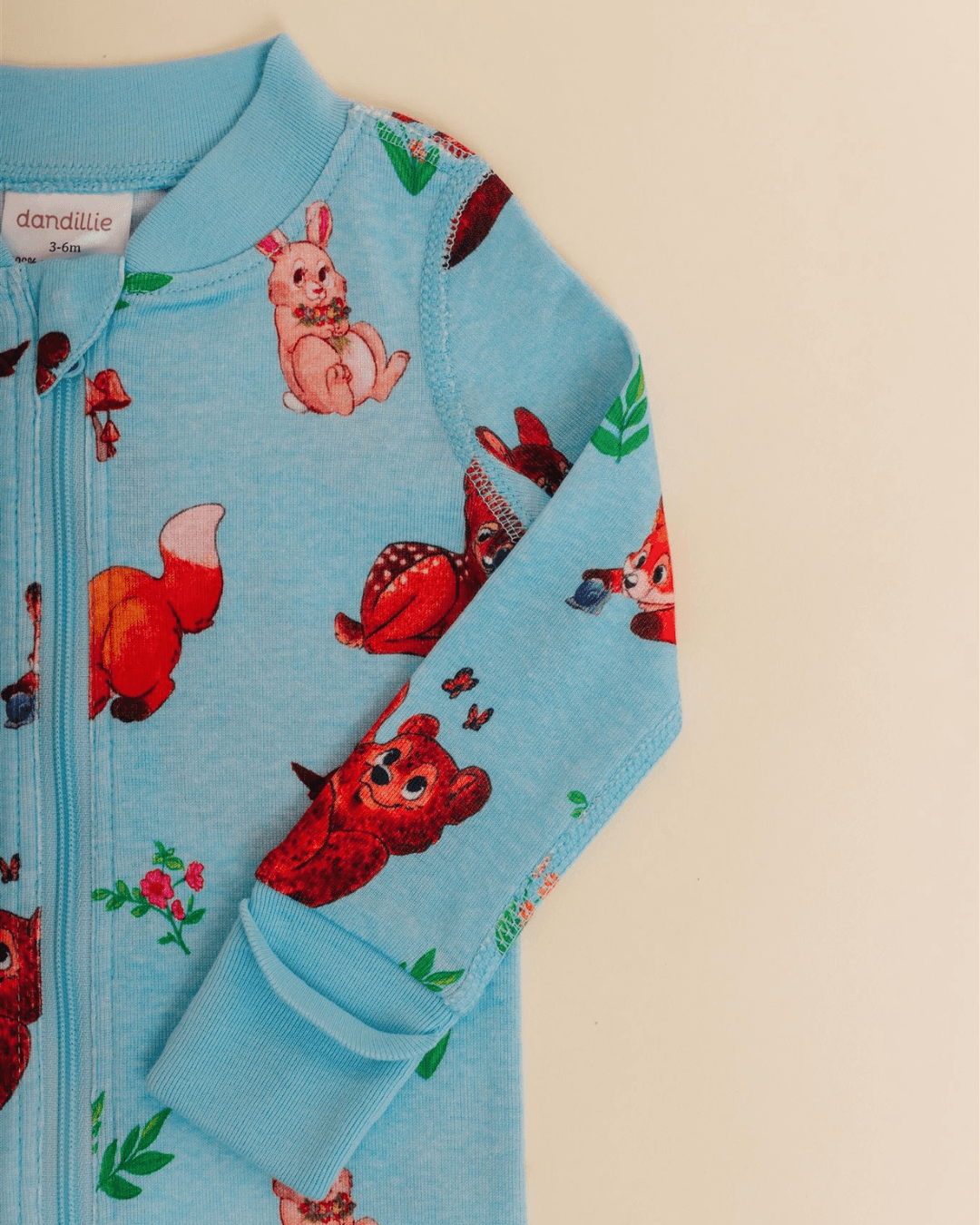 Close-up of a light blue children's jacket with colorful animal and nature prints, including a bear, rabbit, and fox, on a plain background.