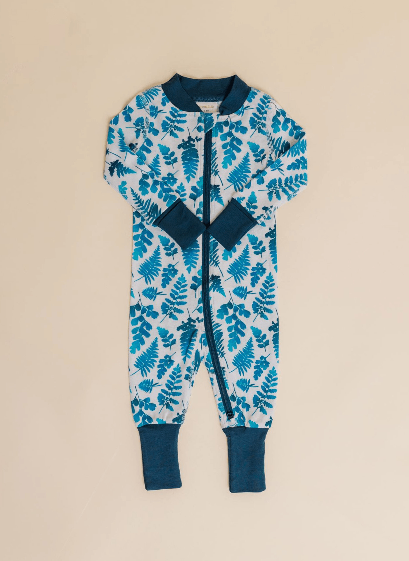 Children's jumpsuit with blue leaf pattern, navy collar, cuffs, and zipper, laid flat on a beige background.