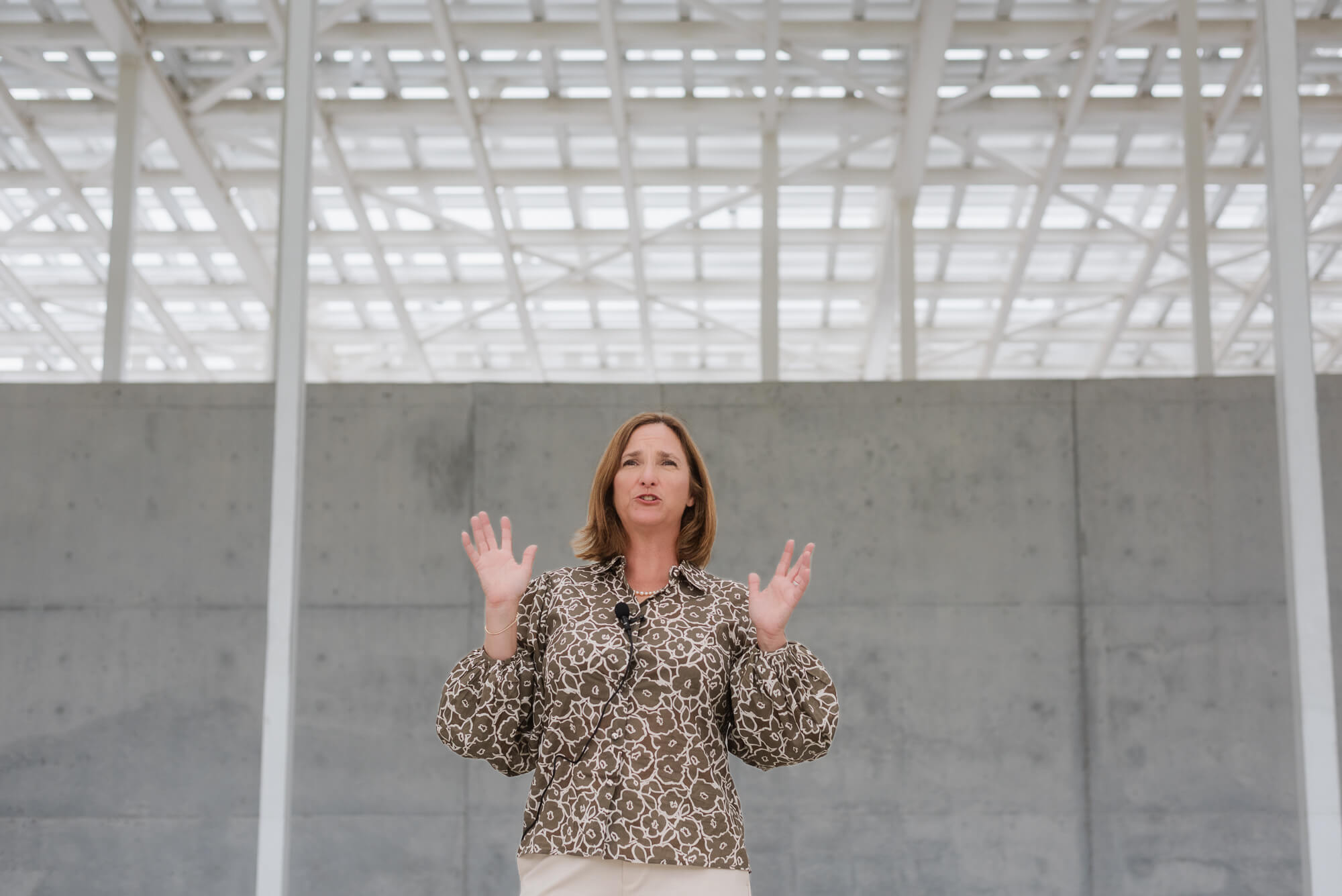 Woman standing indoors with arms raised, wearing a leopard print blouse, in a modern building with glass ceiling.
