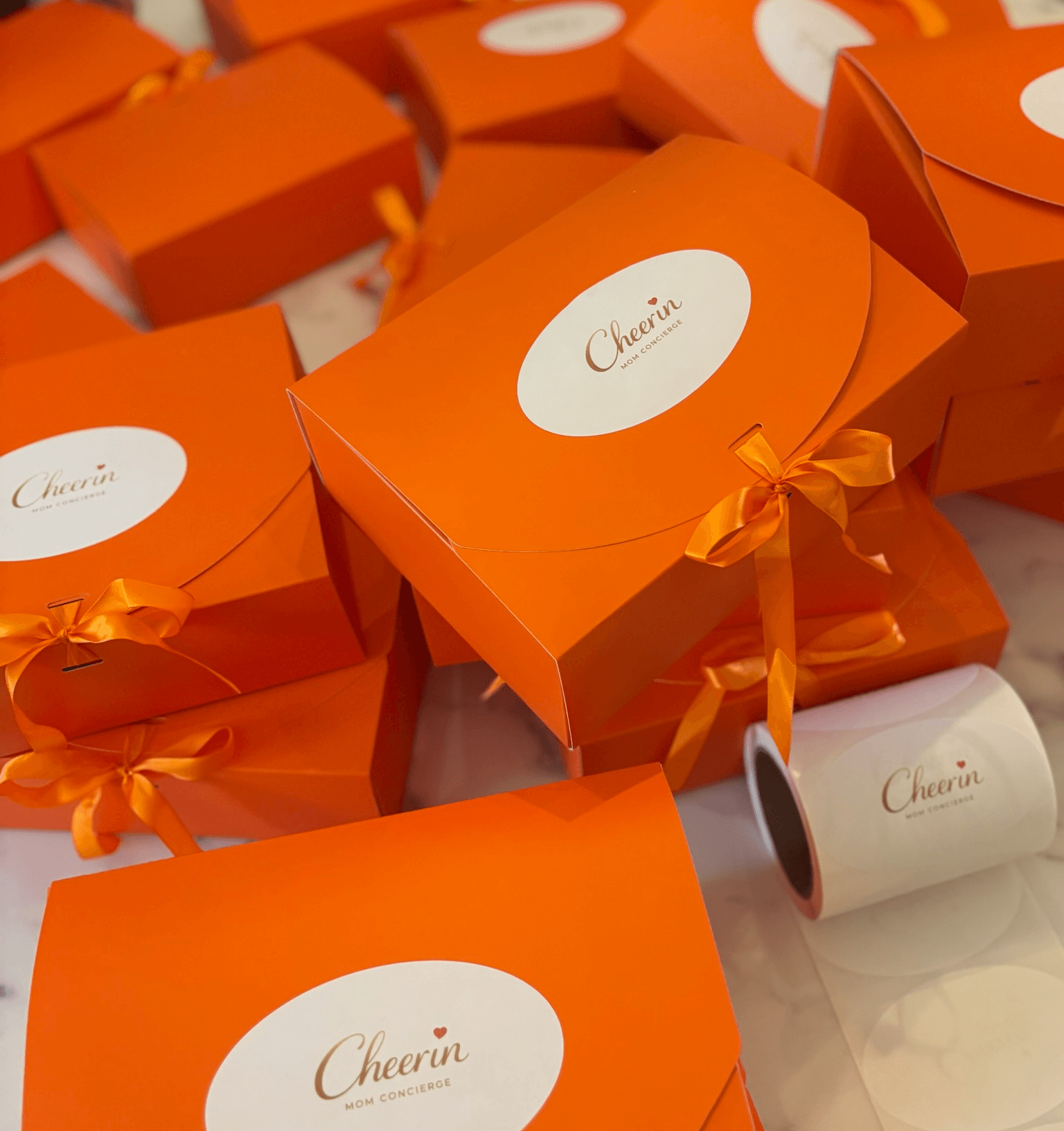 Multiple orange boxes with white oval labels and orange ribbons on a surface.