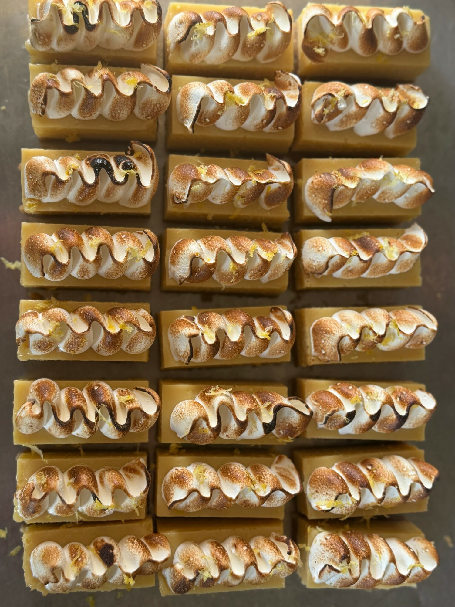 Multiple caramel and nut-topped candies arranged in rows, with a glossy caramel coating and nuts on top.
