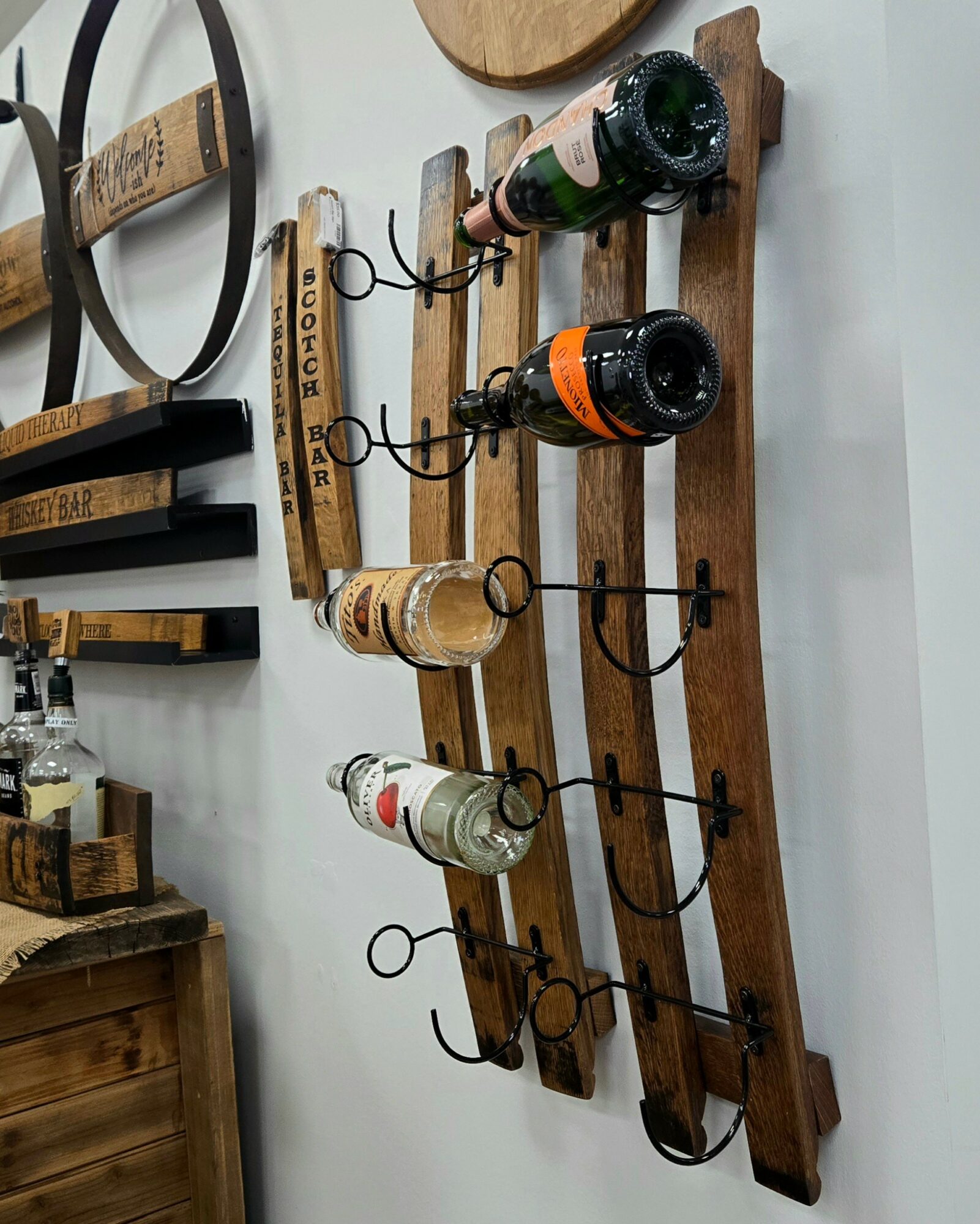 Wooden wine rack holding four bottles, mounted on a white wall, with hooks below for glasses.